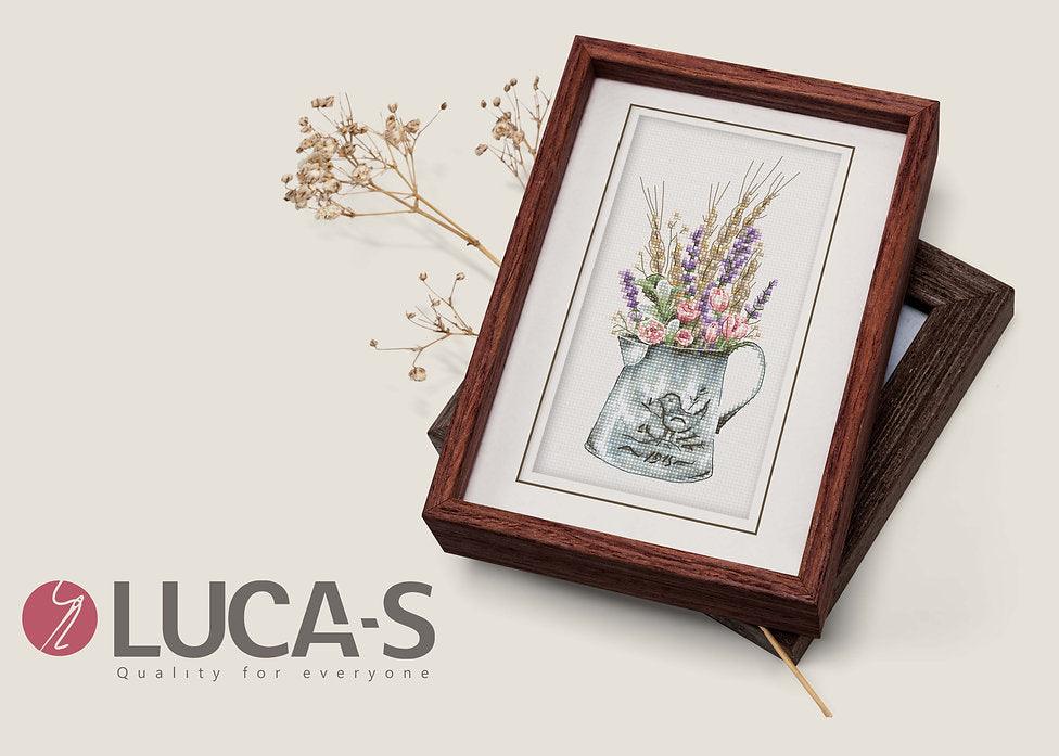 A counted cross-stitch kit featuring a bouquet of lavender and roses in a watering can, showcasing vibrant colors and intricate design.