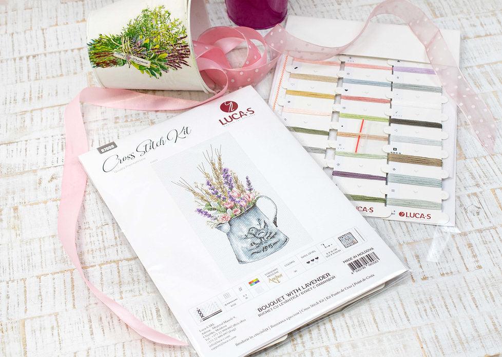 A counted cross-stitch kit featuring a bouquet of lavender and roses in a watering can, showcasing vibrant colors and intricate design.