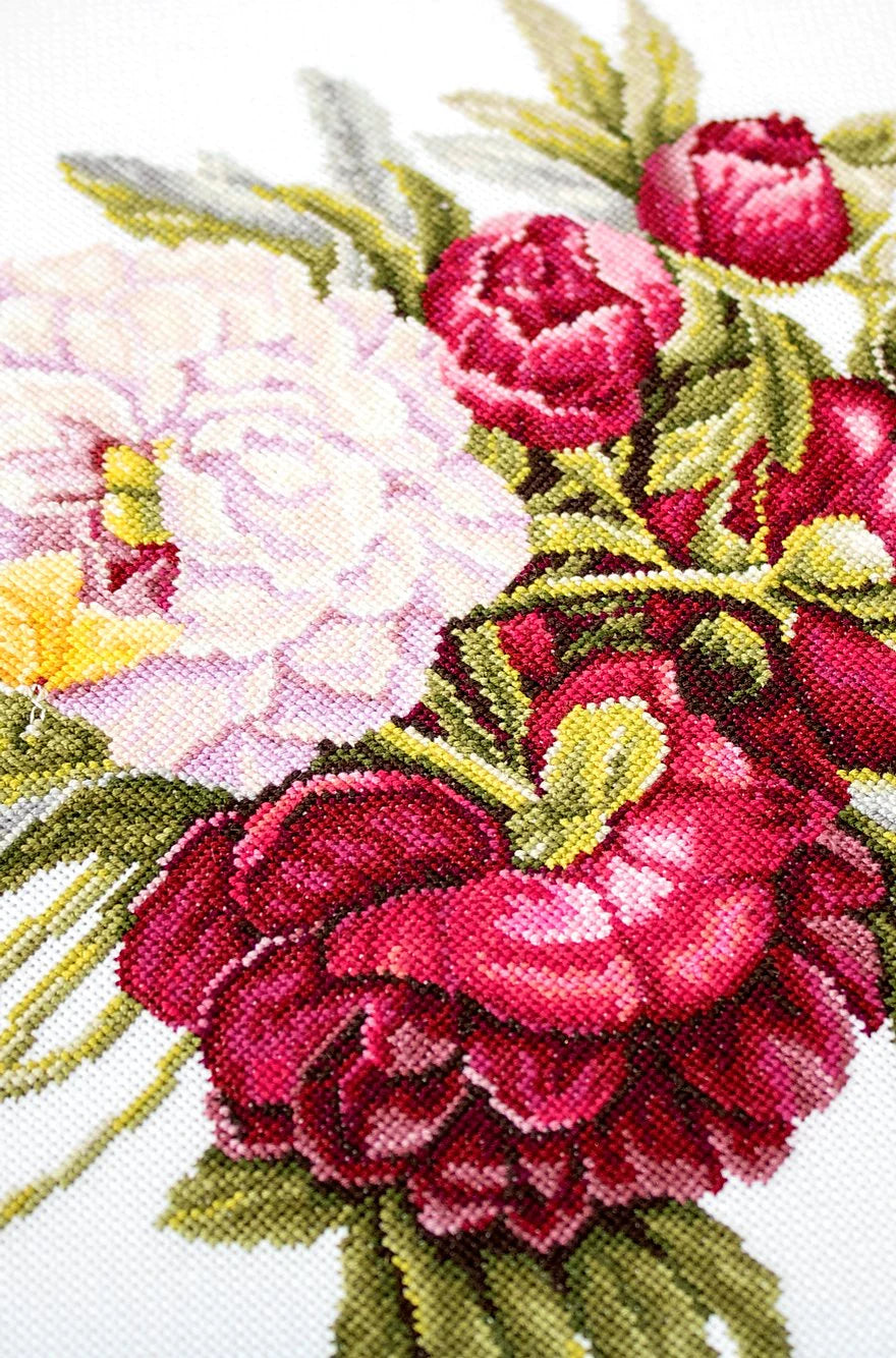 A counted cross-stitch kit featuring a beautiful peony bouquet design, including canvas, colorful threads, needle, and instructions.