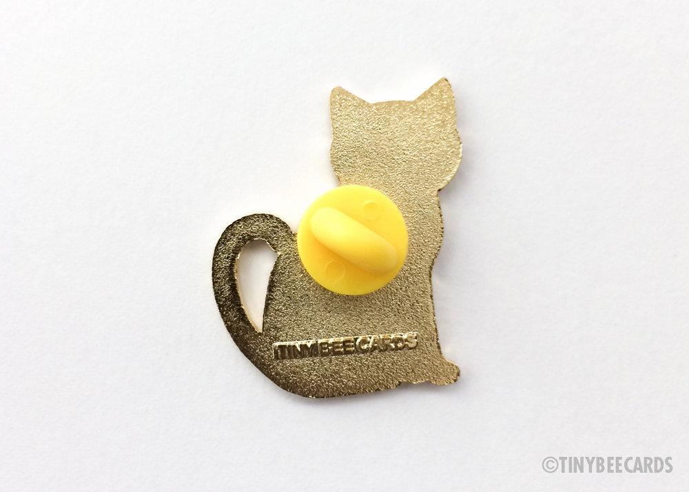 A cute enamel pin featuring a happy black cat with the text 'Feline Good' in a gold border, perfect for cat lovers.