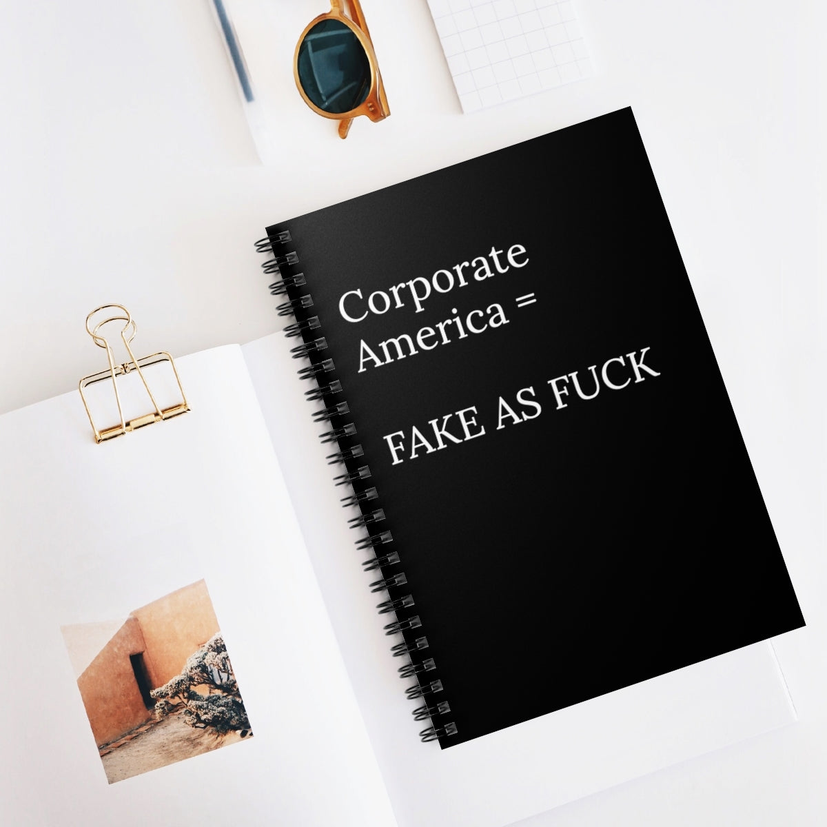 A humorous spiral notebook titled 'Corporate America Equals Fake As Fuck' with ruled line pages, perfect for office use.