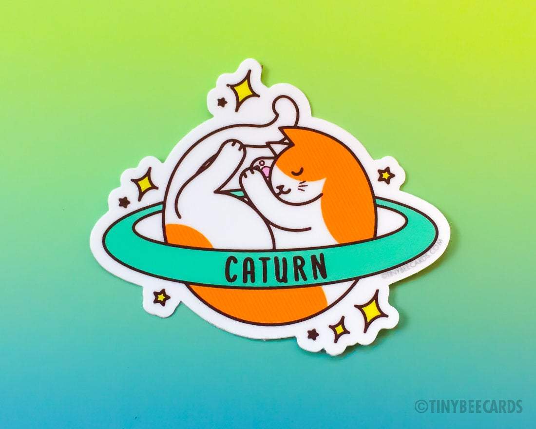 Cute Cosmic Cat Vinyl Sticker featuring an orange and white cat planet with a ring, showcasing the pun 'Caturn'.