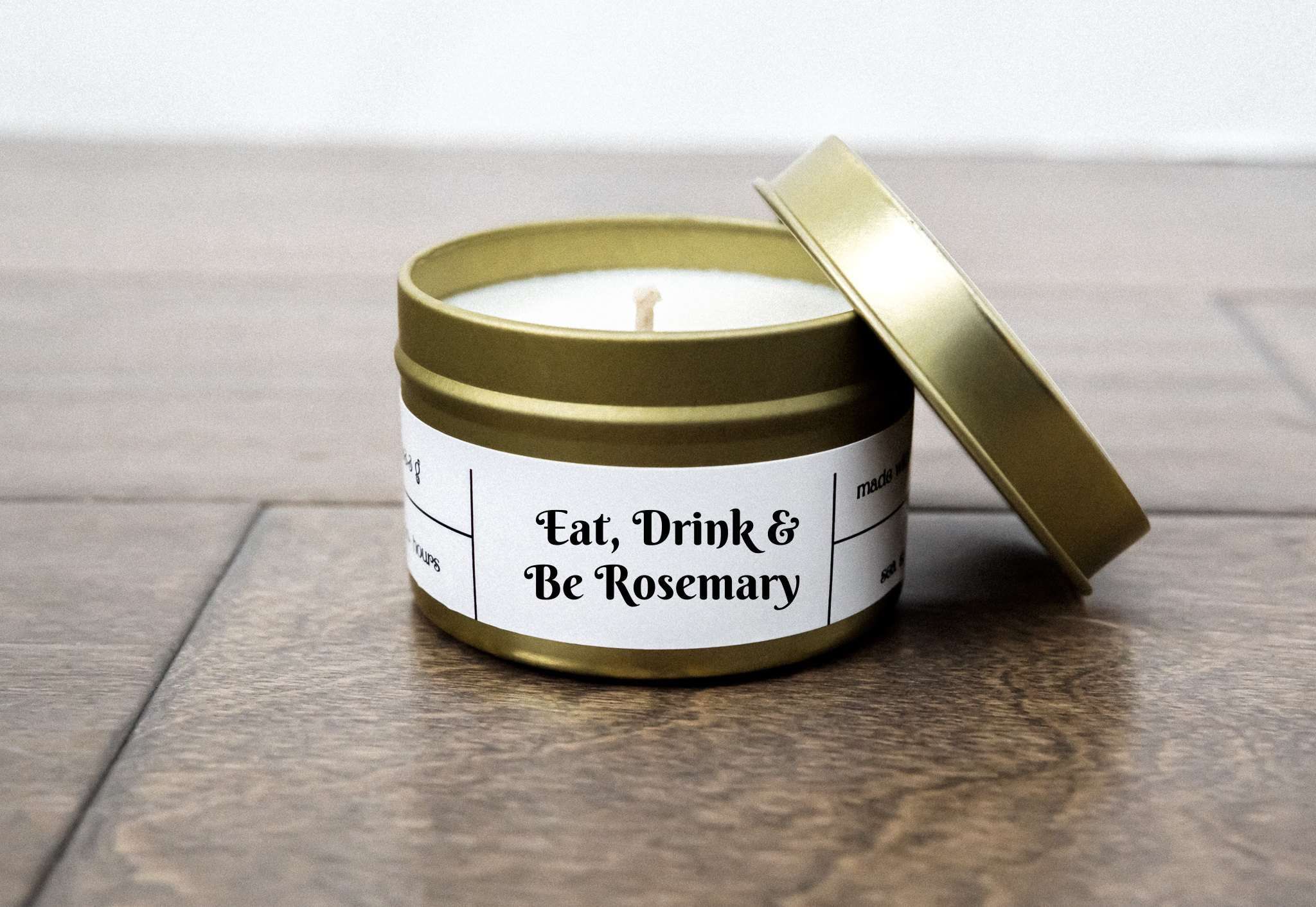 A gold tin jar containing the Eat, Drink, & Be Rosemary Gold Travel Candle, showcasing its elegant design and natural ingredients.