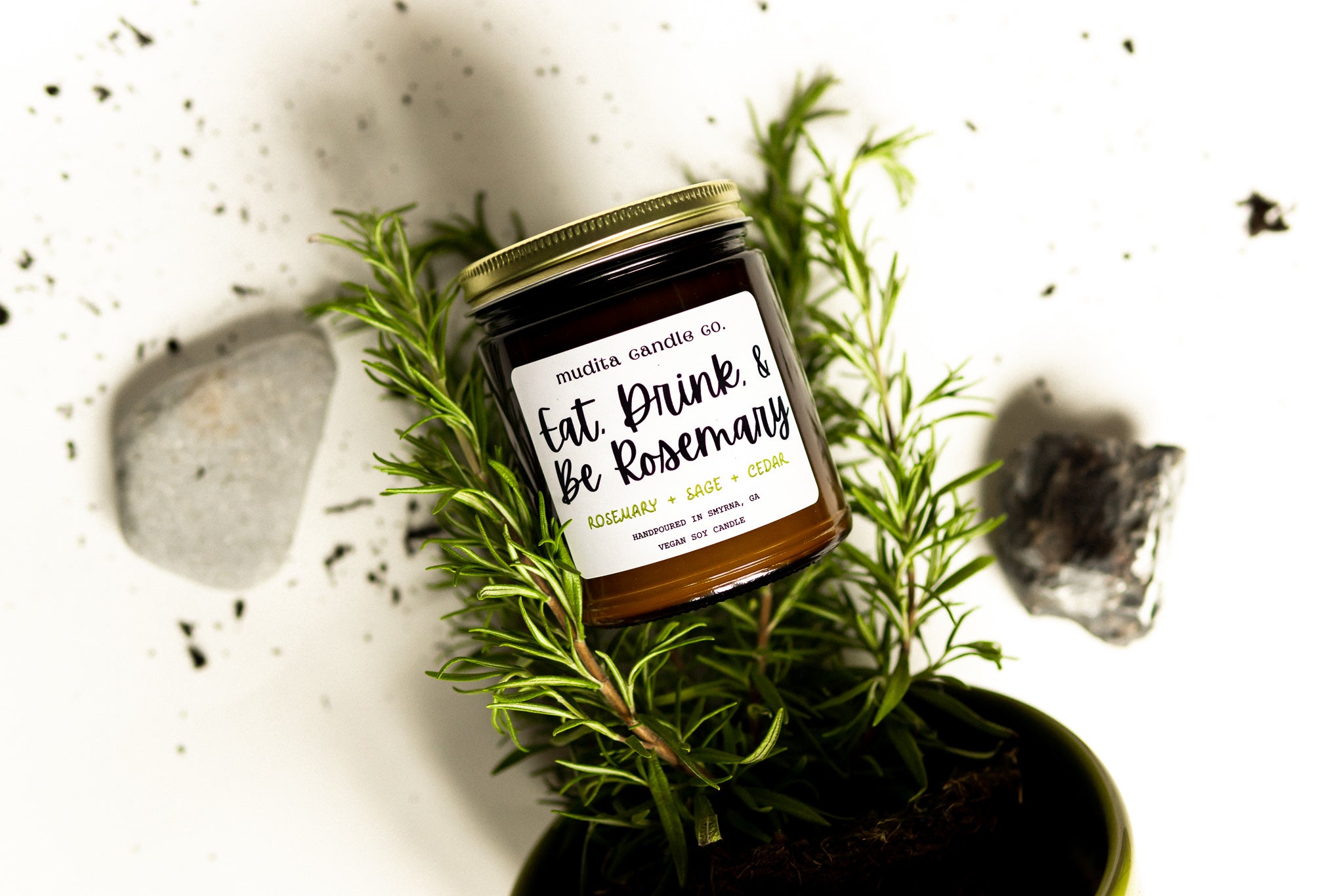 A beautifully crafted 9oz amber glass candle jar with a gold metal lid, featuring the scent 'Eat, Drink, & Be Rosemary' with notes of rosemary, sage, and cedar.