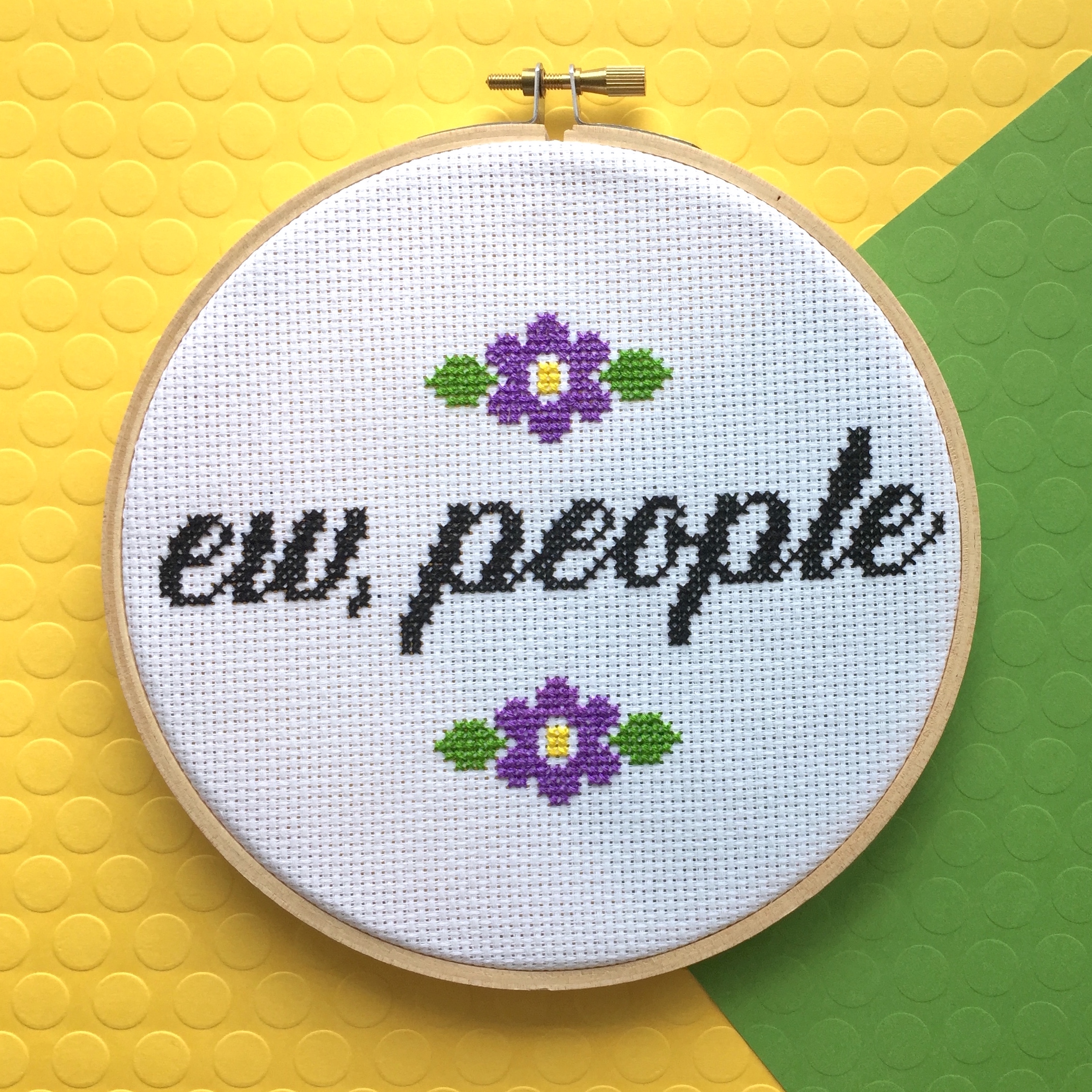 A colorful counted cross stitch kit featuring the phrase 'Ew, People' in cursive surrounded by floral designs, complete with all necessary supplies.