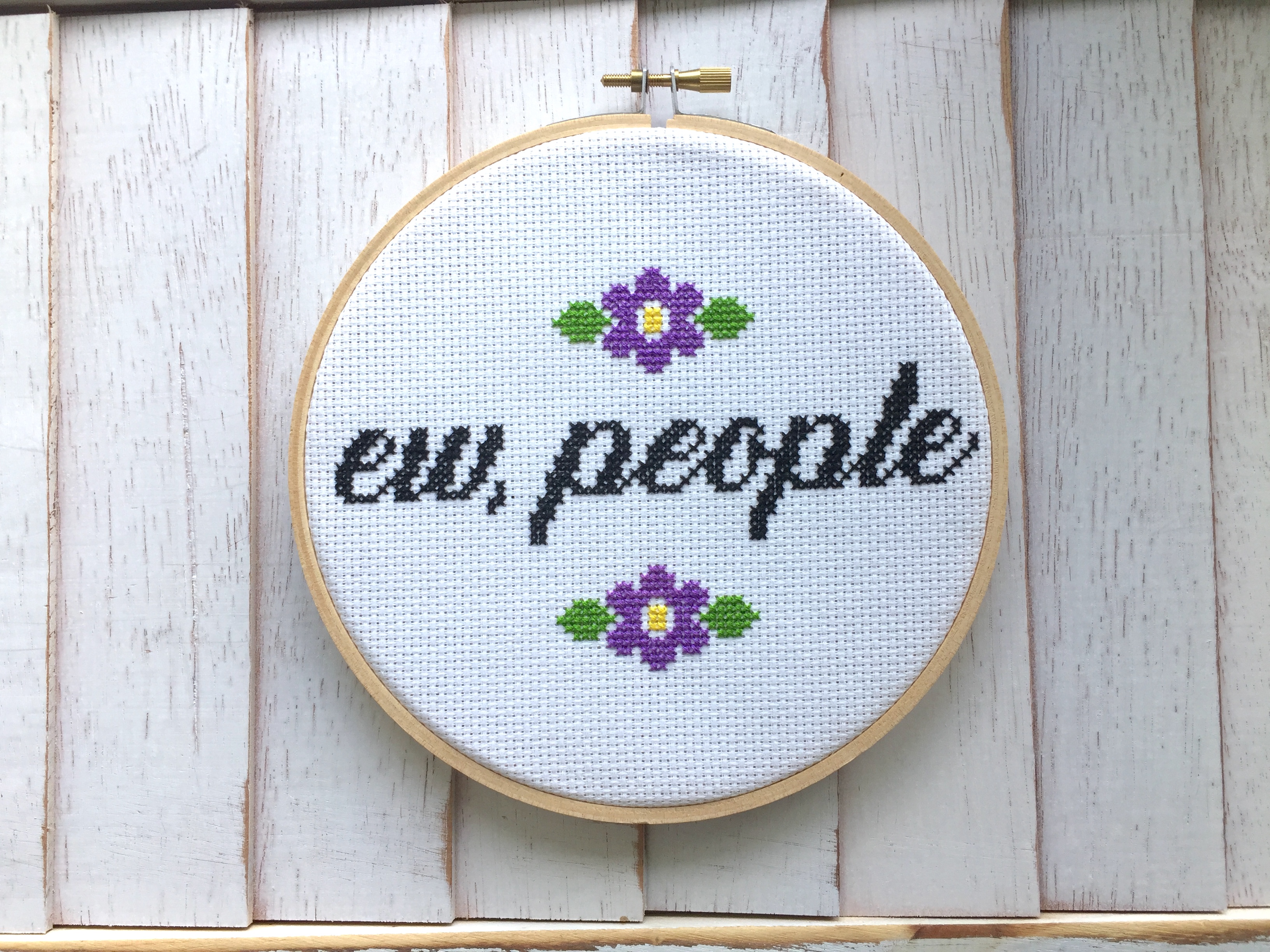 A colorful counted cross stitch kit featuring the phrase 'Ew, People' in cursive surrounded by floral designs, complete with all necessary supplies.