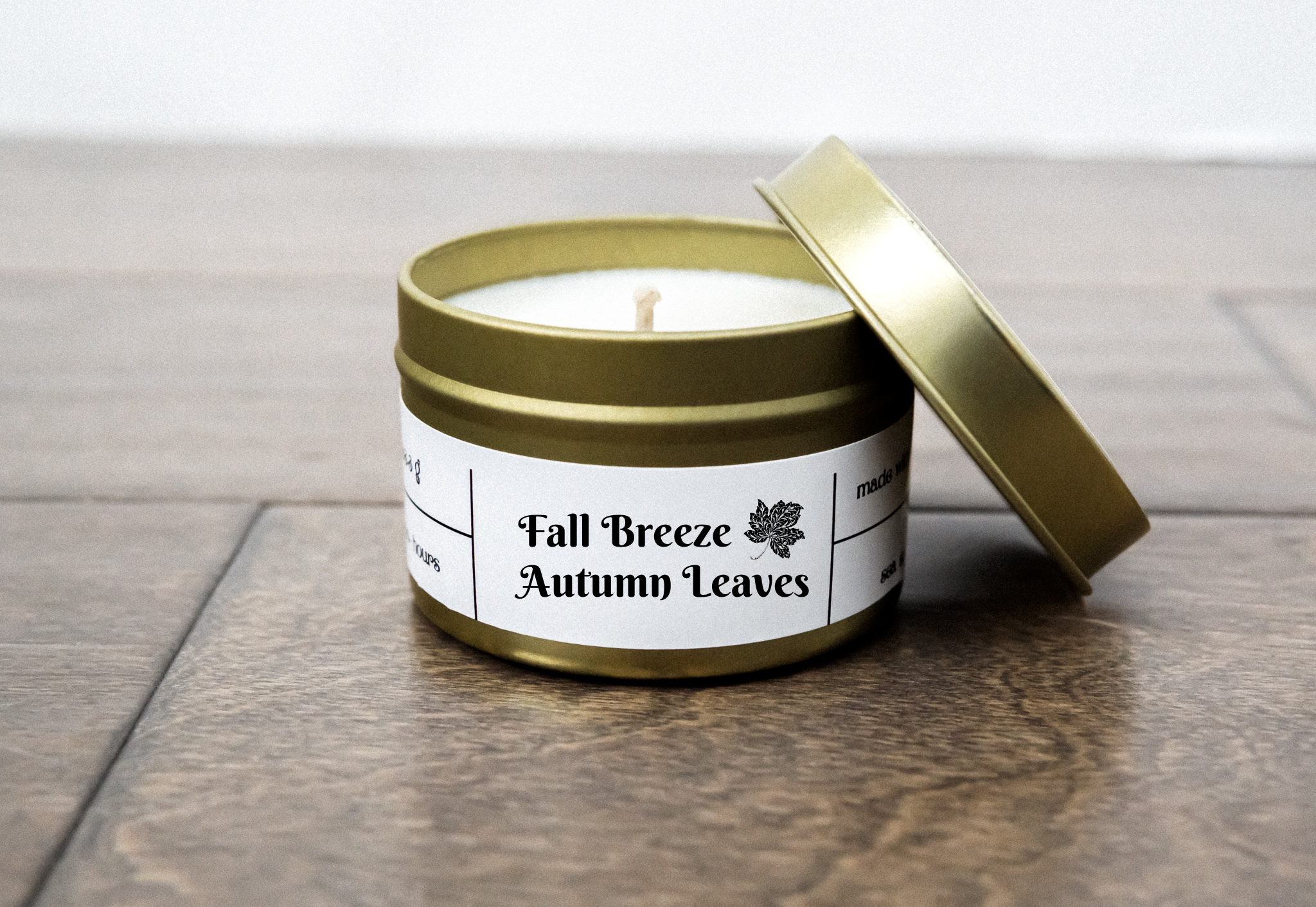 A gold travel candle in a tin jar, featuring a warm autumn-themed label, surrounded by colorful autumn leaves.