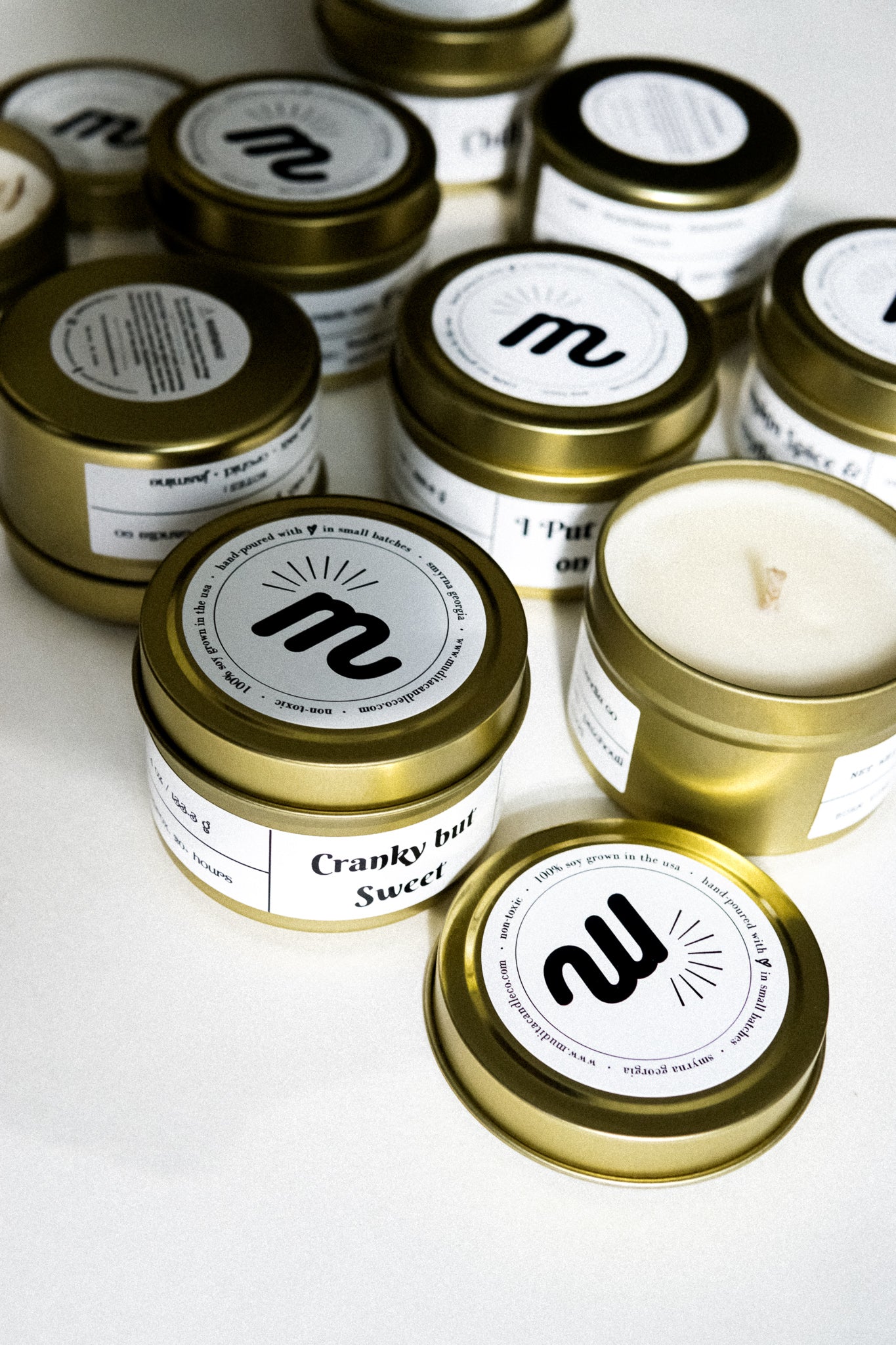 A gold travel candle in a tin jar, featuring a warm autumn-themed label, surrounded by colorful autumn leaves.