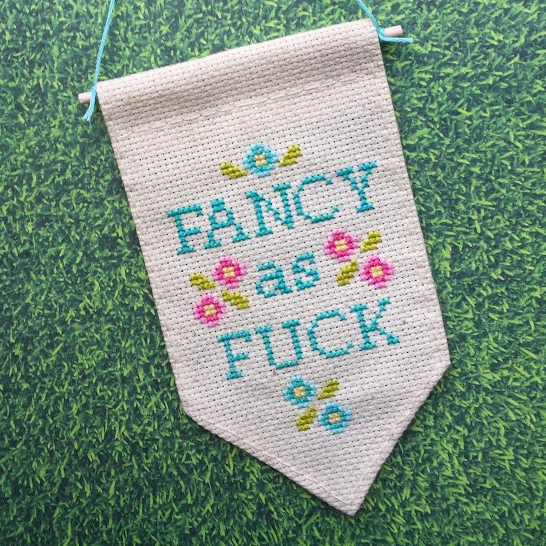 Fancy as F*ck Tiny Banner Counted Cross Stitch Kit featuring pastel threads on oatmeal fabric.