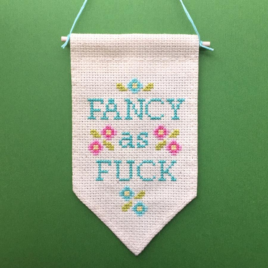 Fancy as F*ck Tiny Banner Counted Cross Stitch Kit featuring pastel threads on oatmeal fabric.