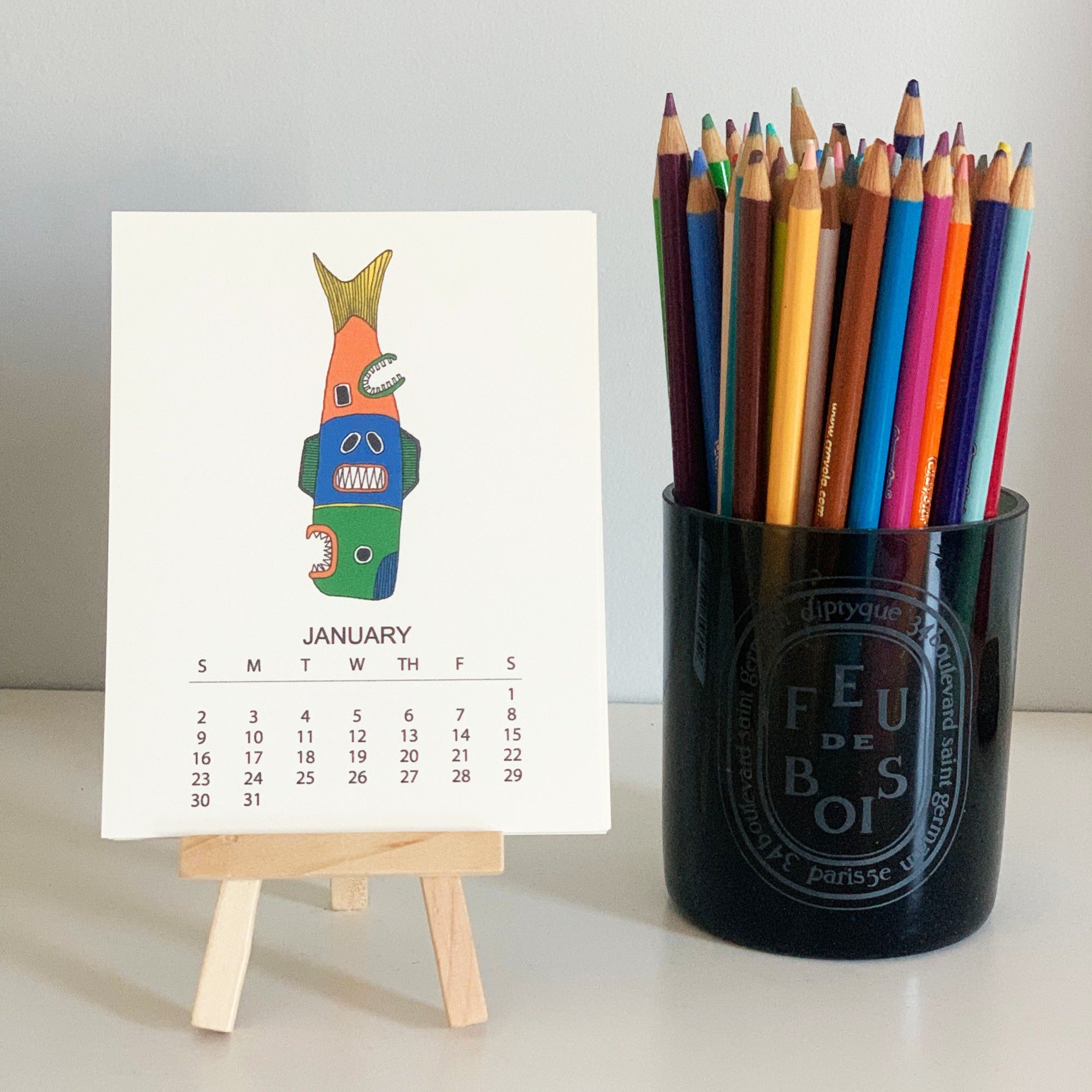 2022 Monthly Desk Calendar featuring original fish totem drawings displayed on a wooden easel.