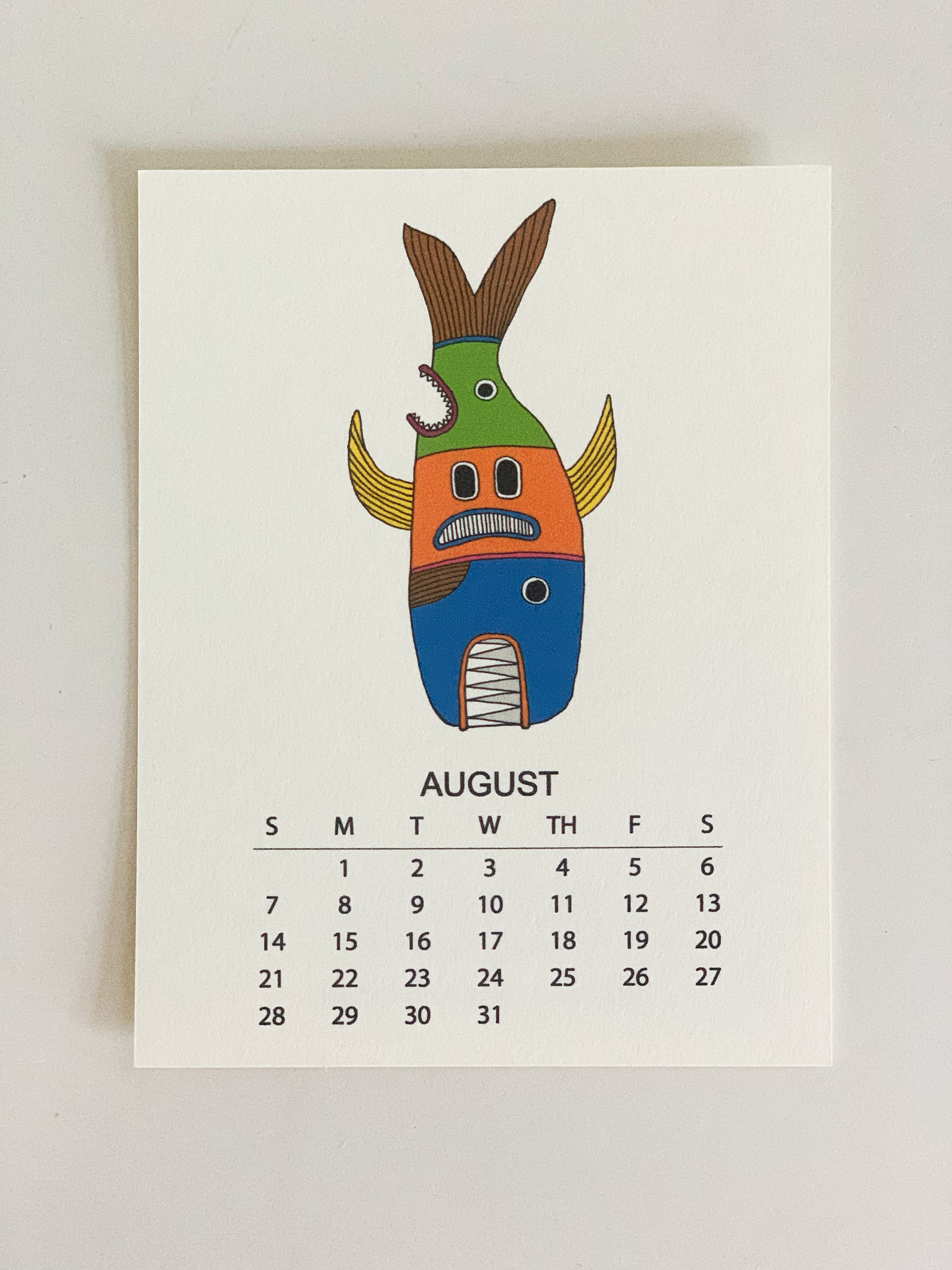 2022 Monthly Desk Calendar featuring original fish totem drawings displayed on a wooden easel.