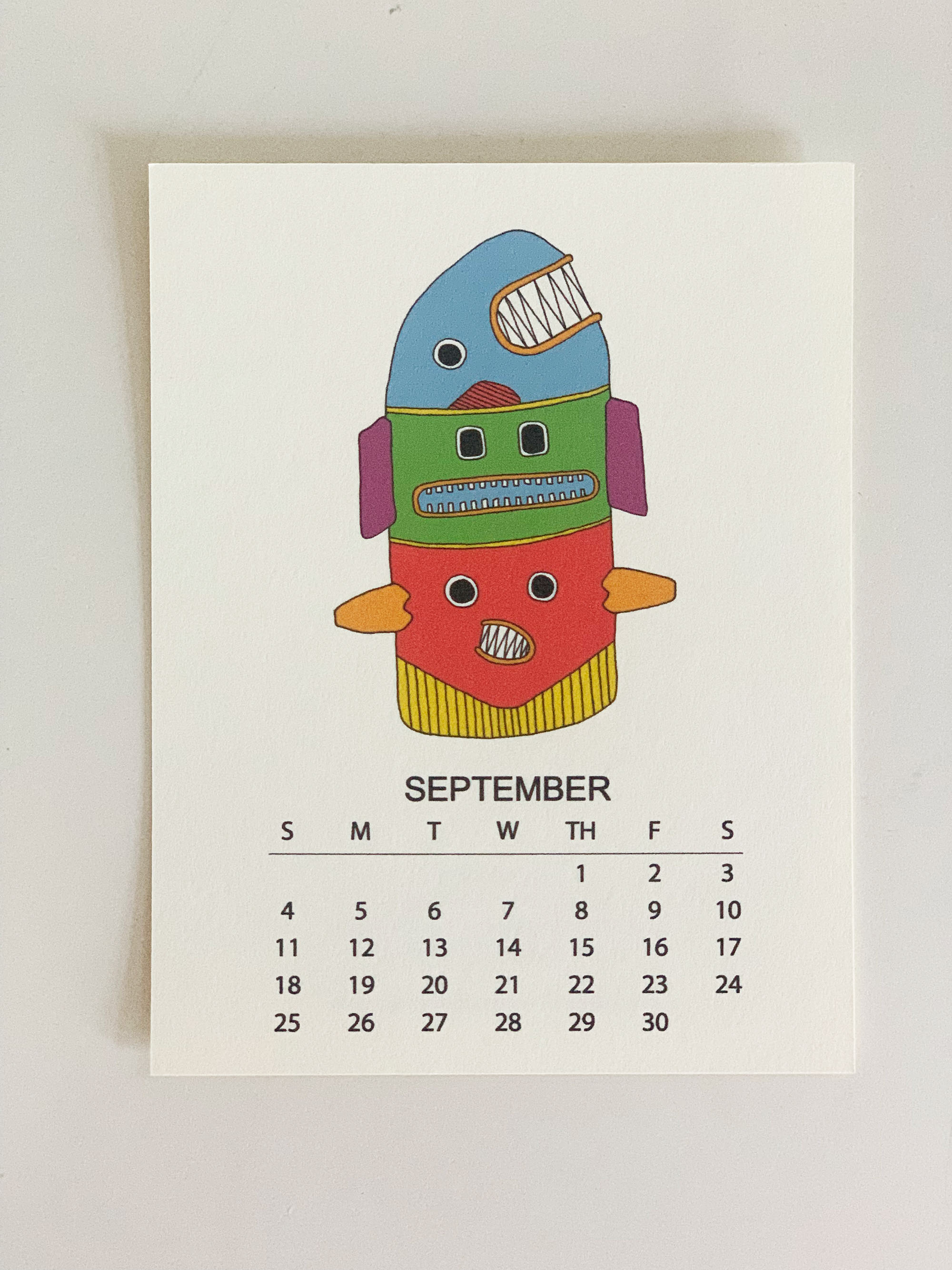 2022 Monthly Desk Calendar featuring original fish totem drawings displayed on a wooden easel.