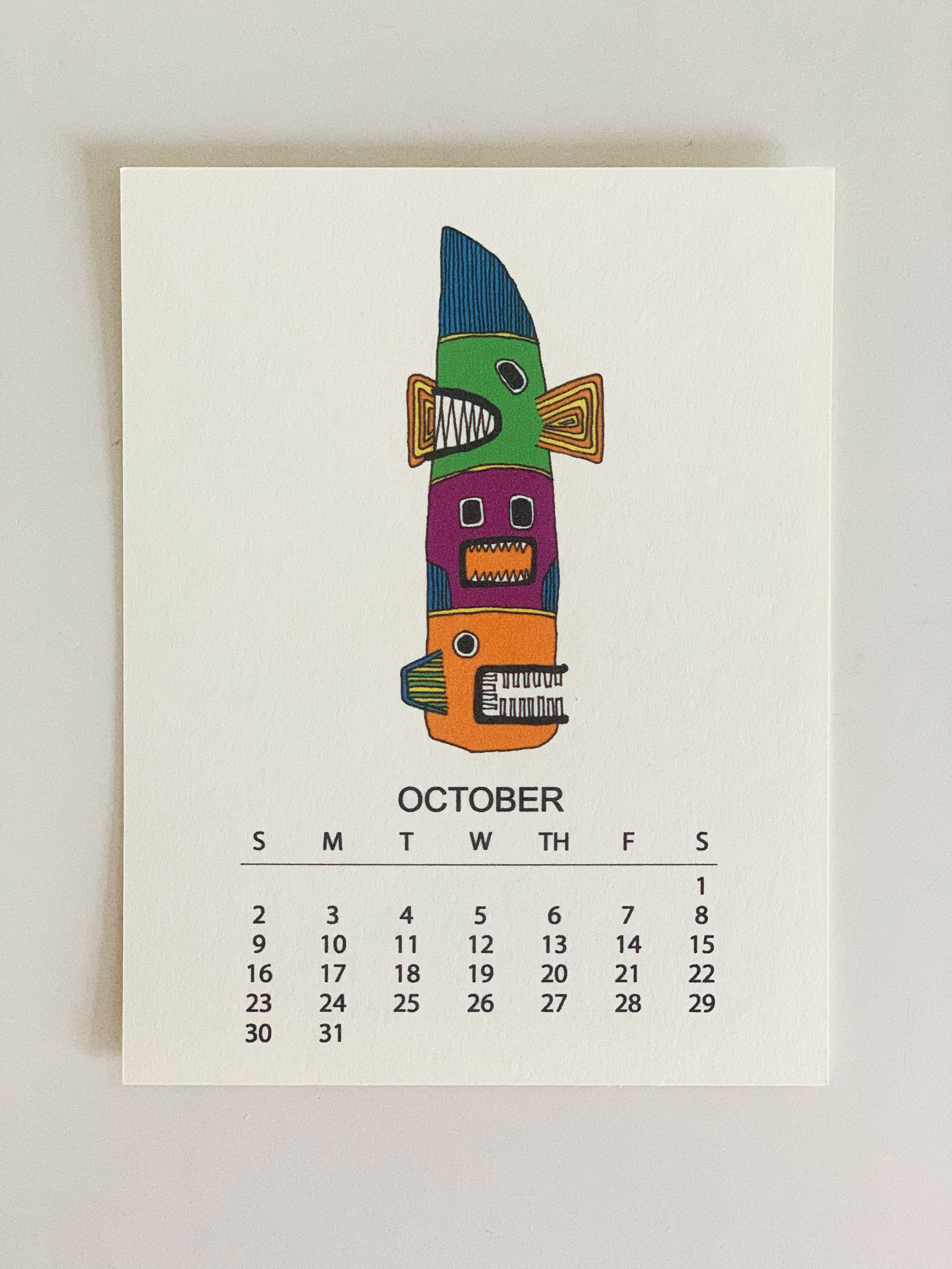 2022 Monthly Desk Calendar featuring original fish totem drawings displayed on a wooden easel.