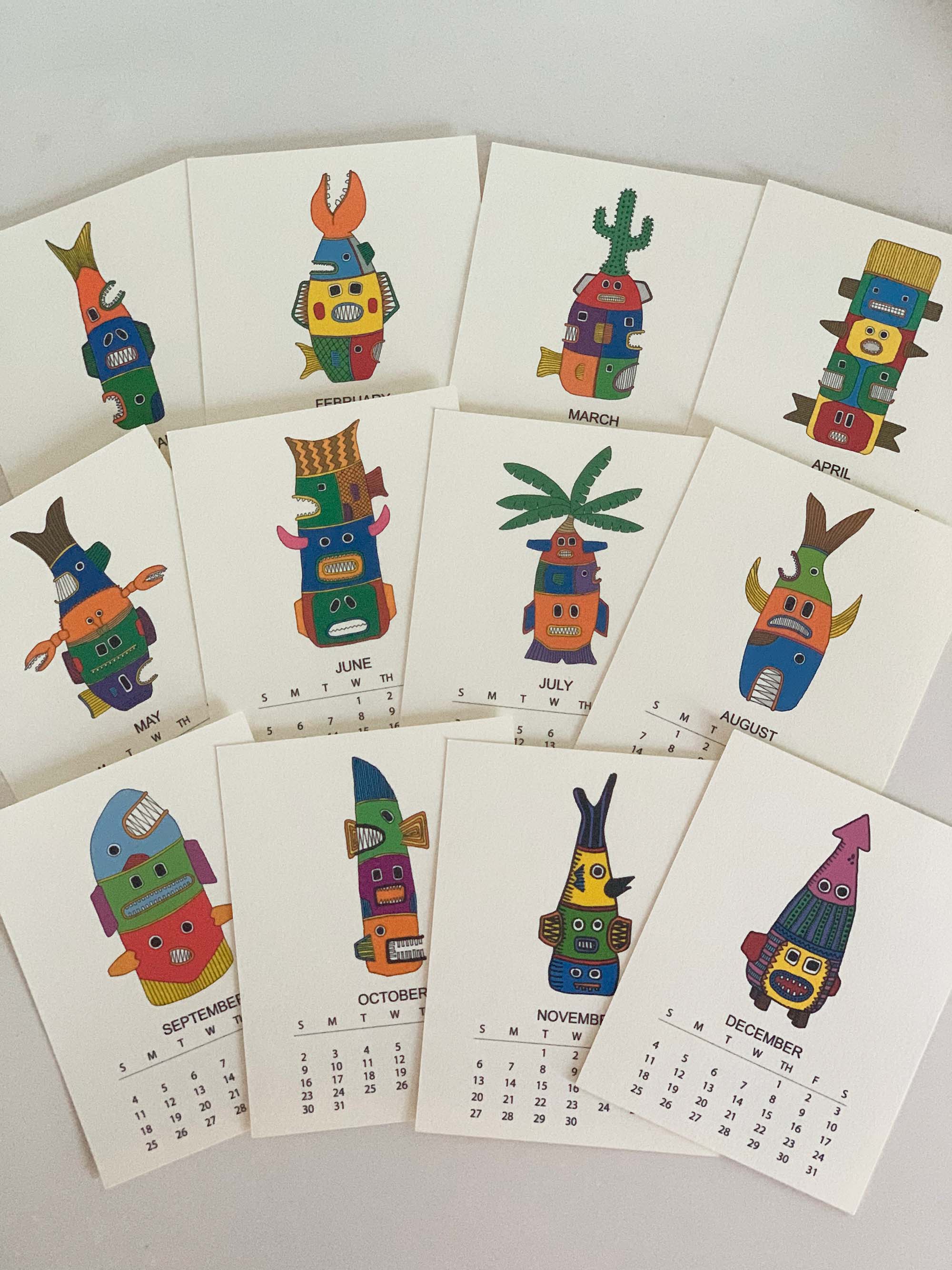 2022 Monthly Desk Calendar featuring original fish totem drawings displayed on a wooden easel.