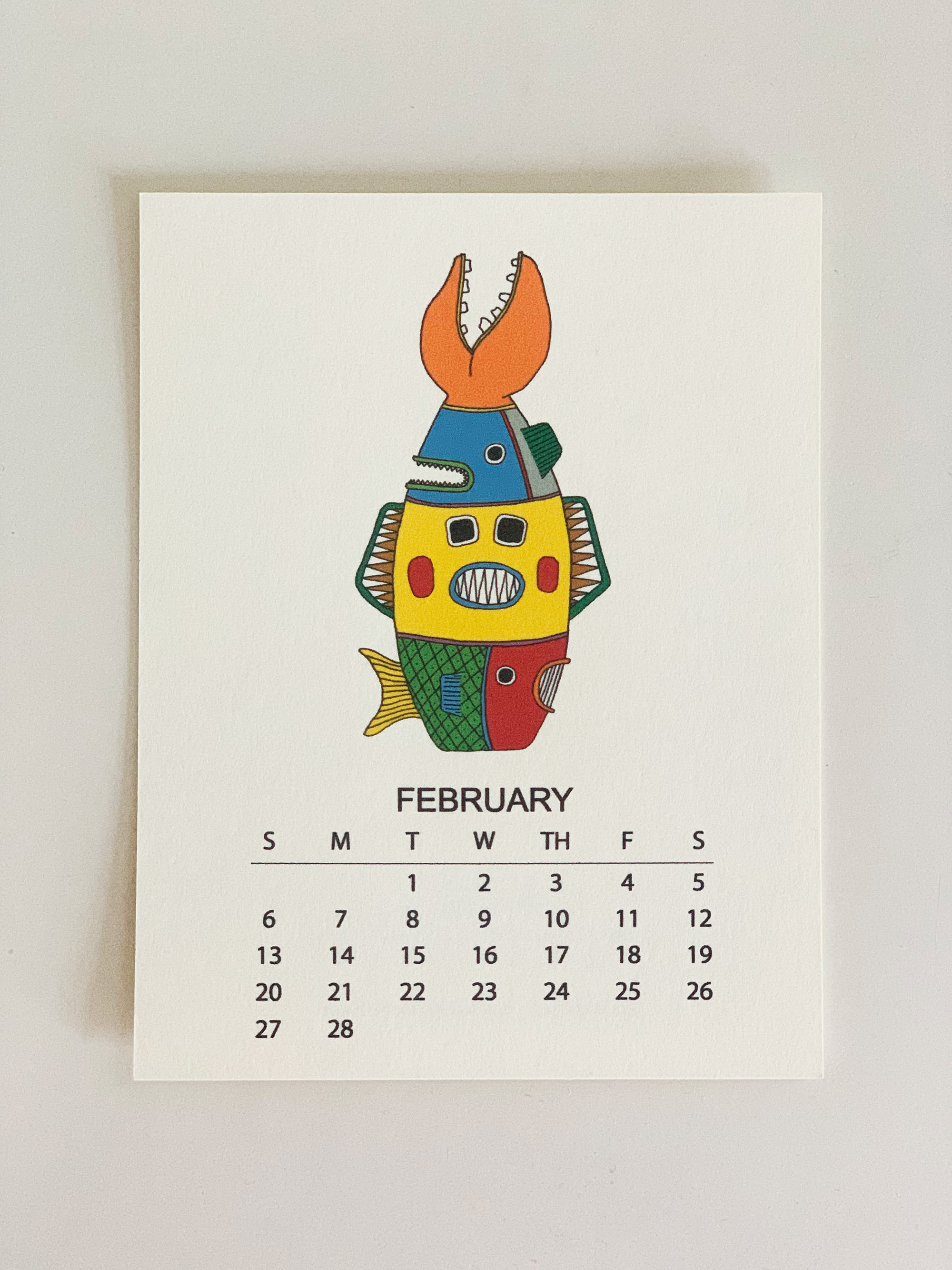 2022 Monthly Desk Calendar featuring original fish totem drawings displayed on a wooden easel.