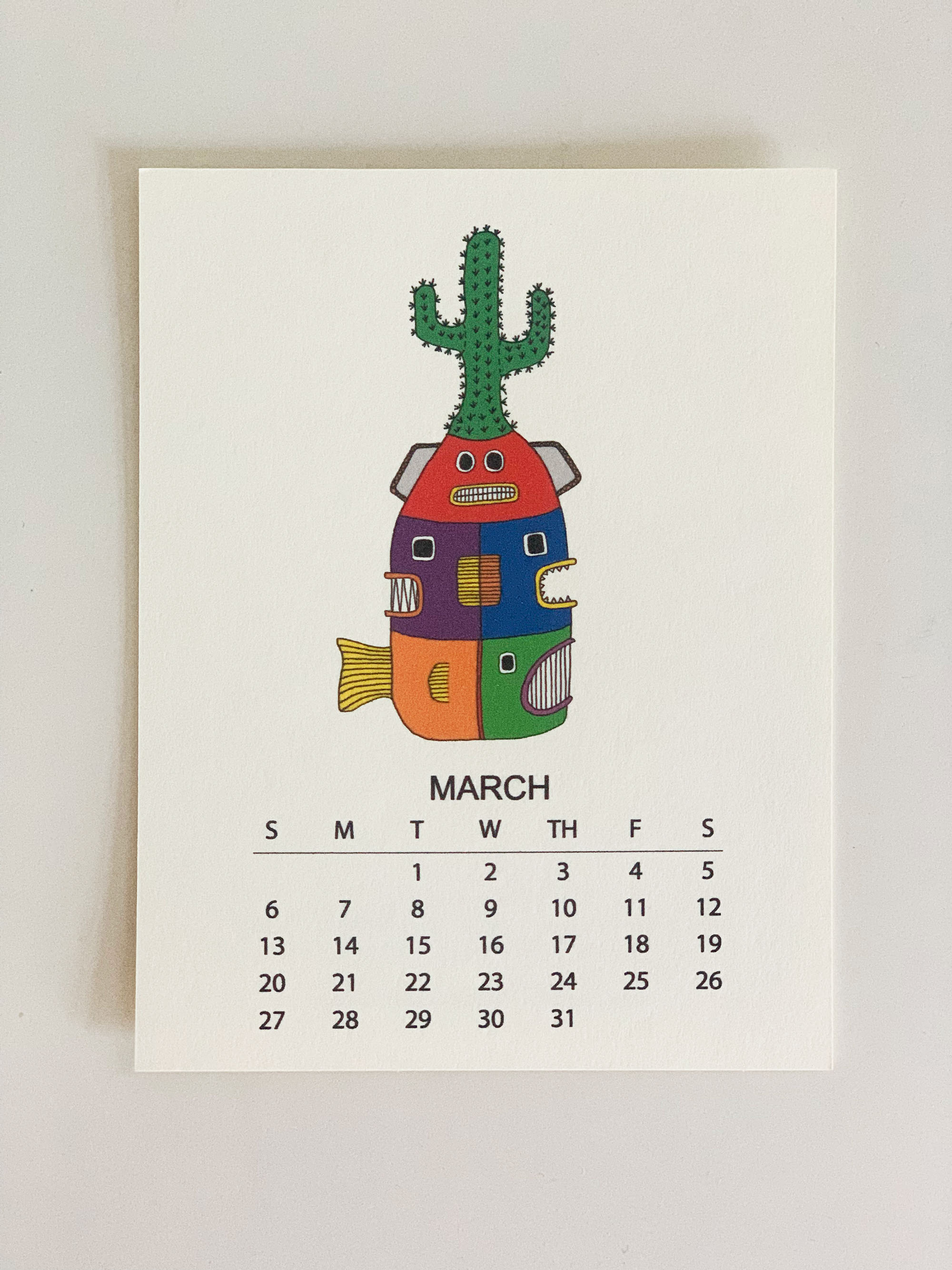 2022 Monthly Desk Calendar featuring original fish totem drawings displayed on a wooden easel.