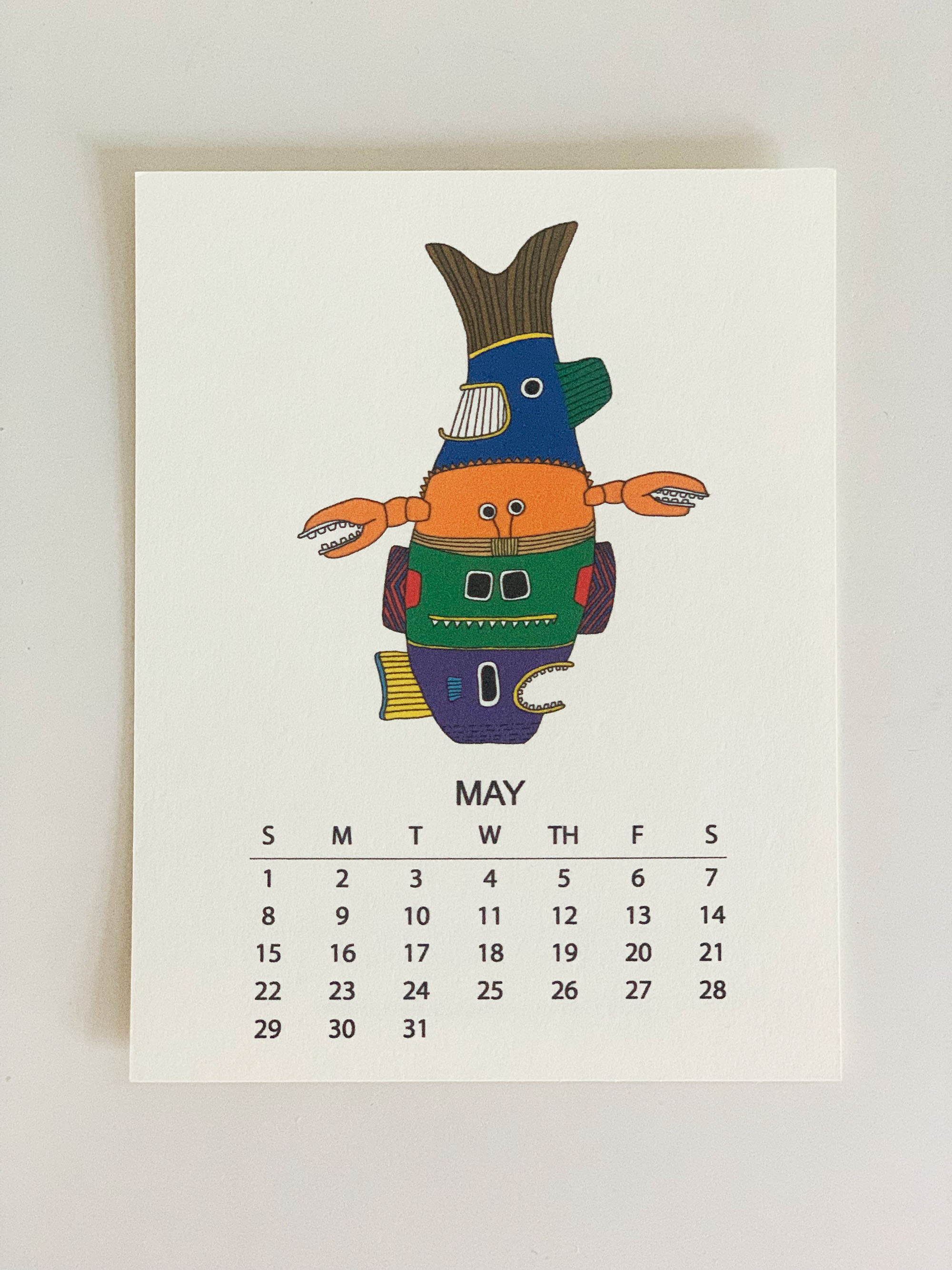 2022 Monthly Desk Calendar featuring original fish totem drawings displayed on a wooden easel.