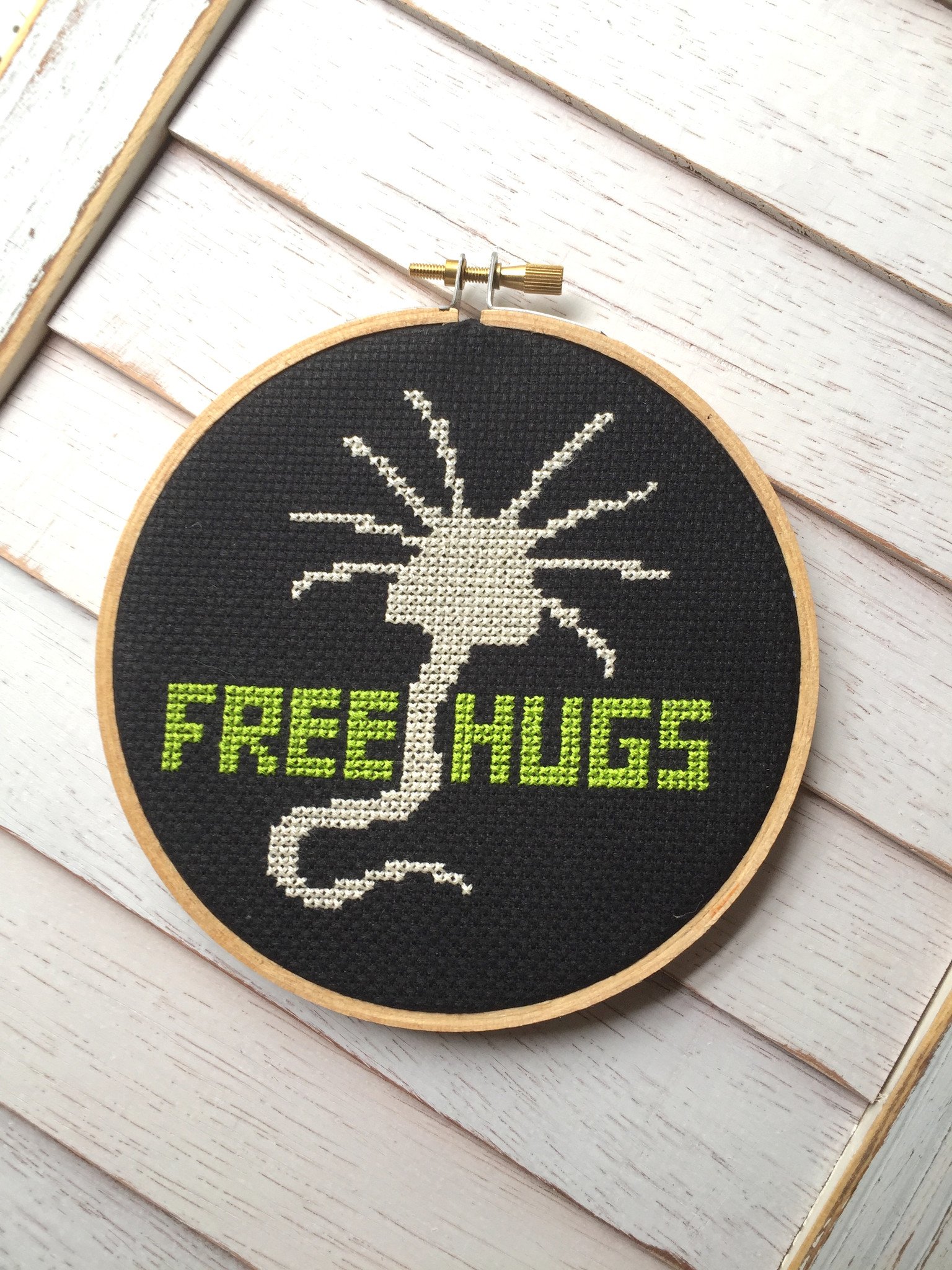 A colorful counted cross stitch kit featuring a whimsical alien character with the text 'Free Hugs', including threads, fabric, and a hoop.