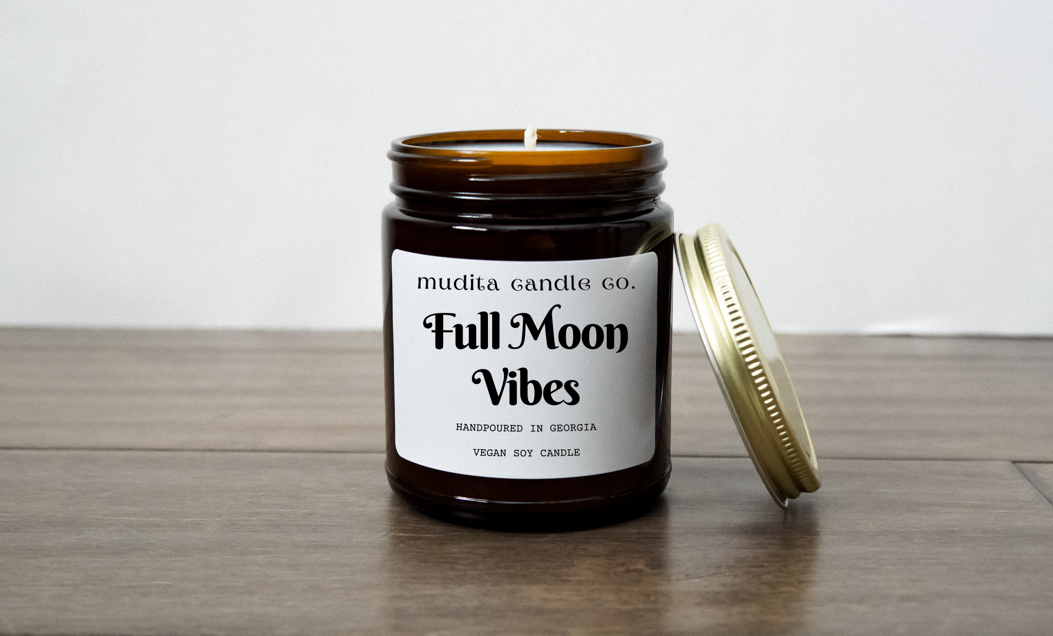 A 9oz amber glass candle jar with a gold metal lid, labeled 'Full Moon Vibes', surrounded by soft candlelight, evoking a serene atmosphere.