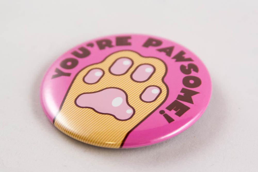 Funny cat paw magnet or pin featuring the phrase 'you're pawsome!' in a playful design.