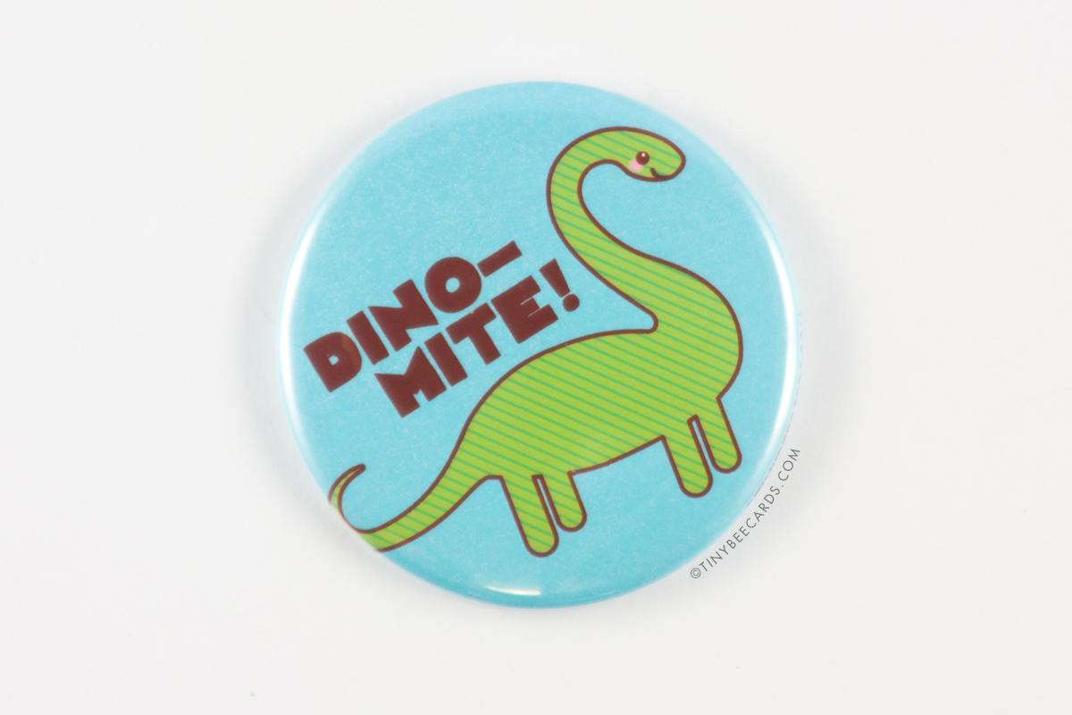 A 2.25-inch round button featuring a cute brontosaurus and the text 'Dino-mite!', available as a magnet, pin, or pocket mirror.