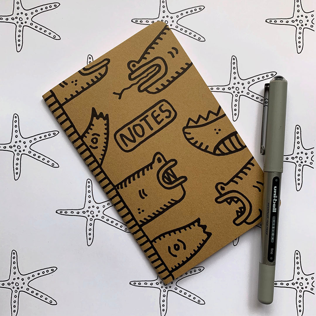 Hand-decorated Moleskine journal with reptilian designs on kraft cover, featuring a beanie-wearing reptile.