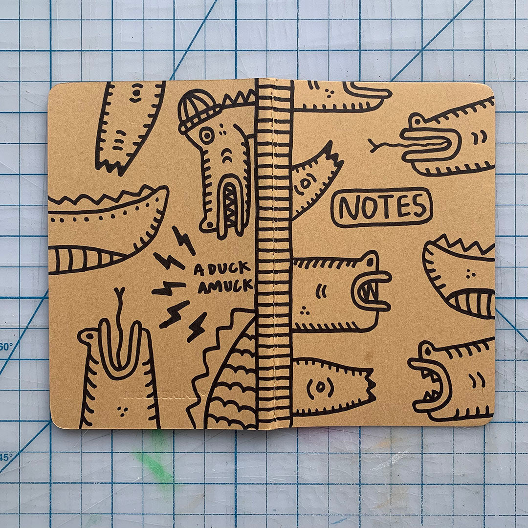 Hand-decorated Moleskine journal with reptilian designs on kraft cover, featuring a beanie-wearing reptile.