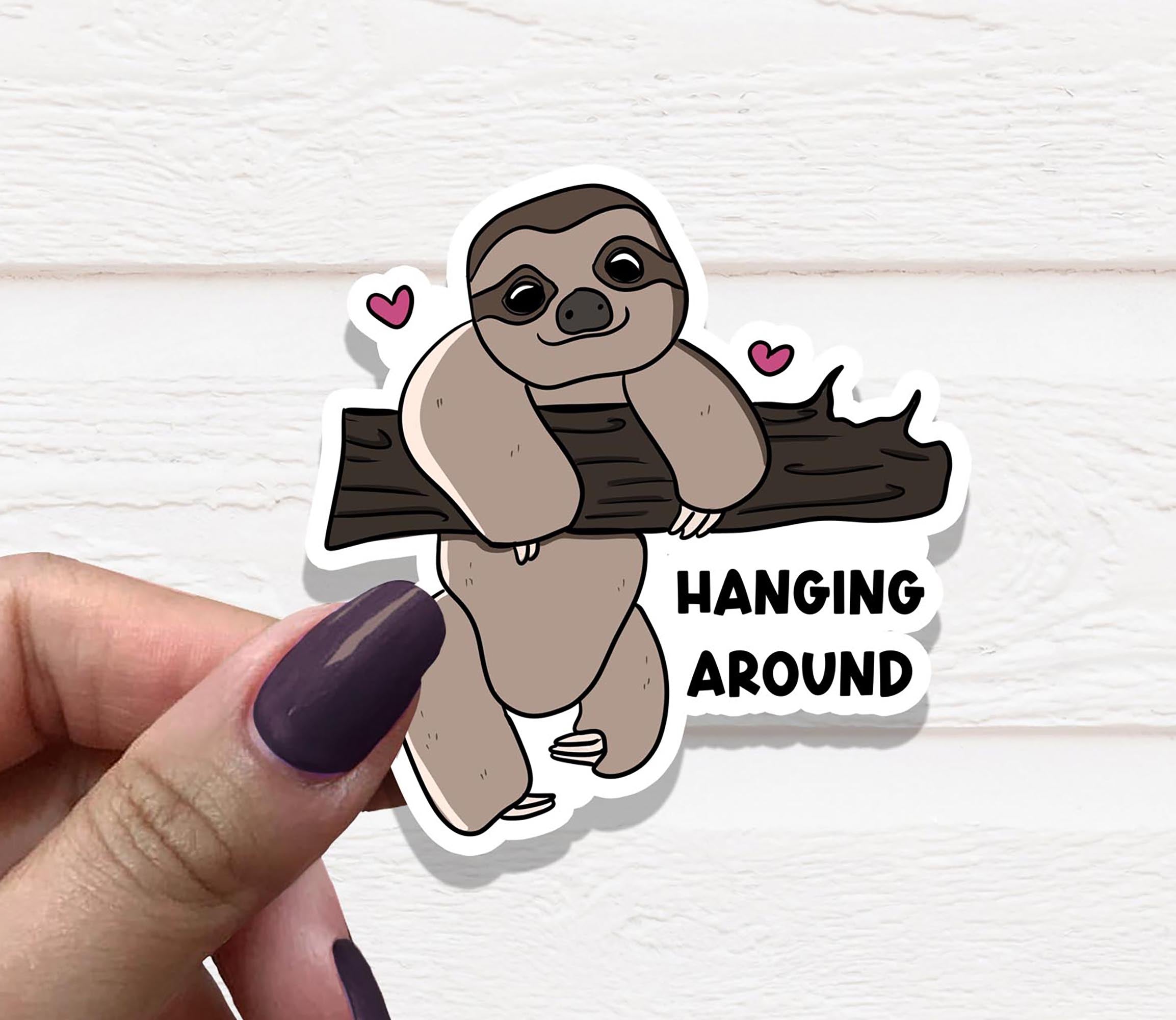 A cute vinyl sticker featuring a sloth hanging from a branch, printed on high-quality matte vinyl with a laminated finish for durability.