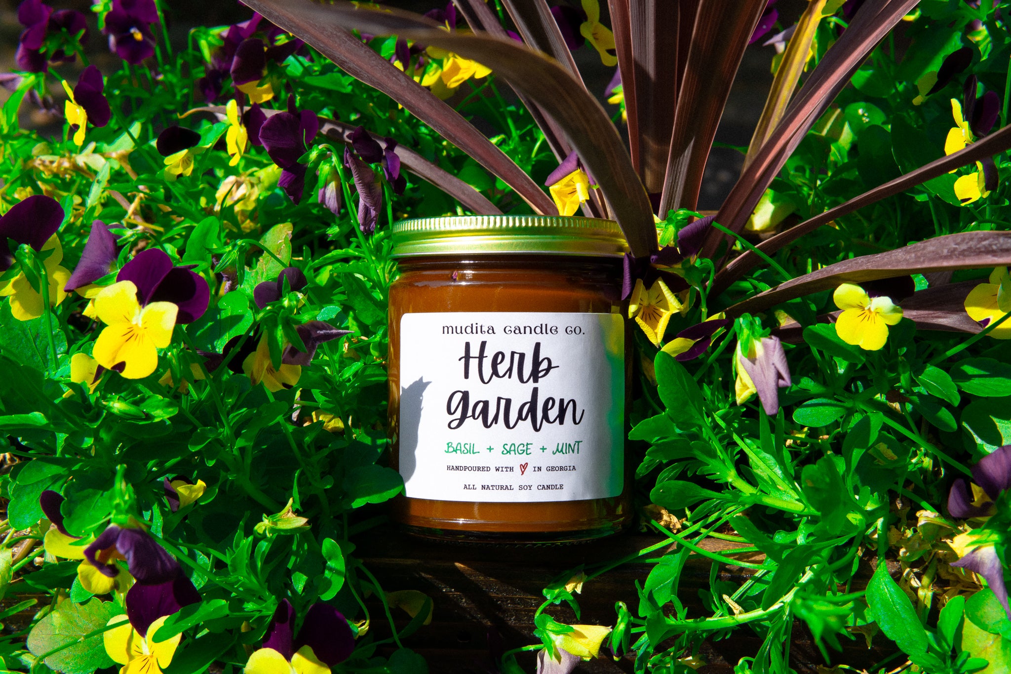 Herb Garden candle in a reusable amber glass jar with a gold lid, featuring a blend of mint, basil, and citrus scents.