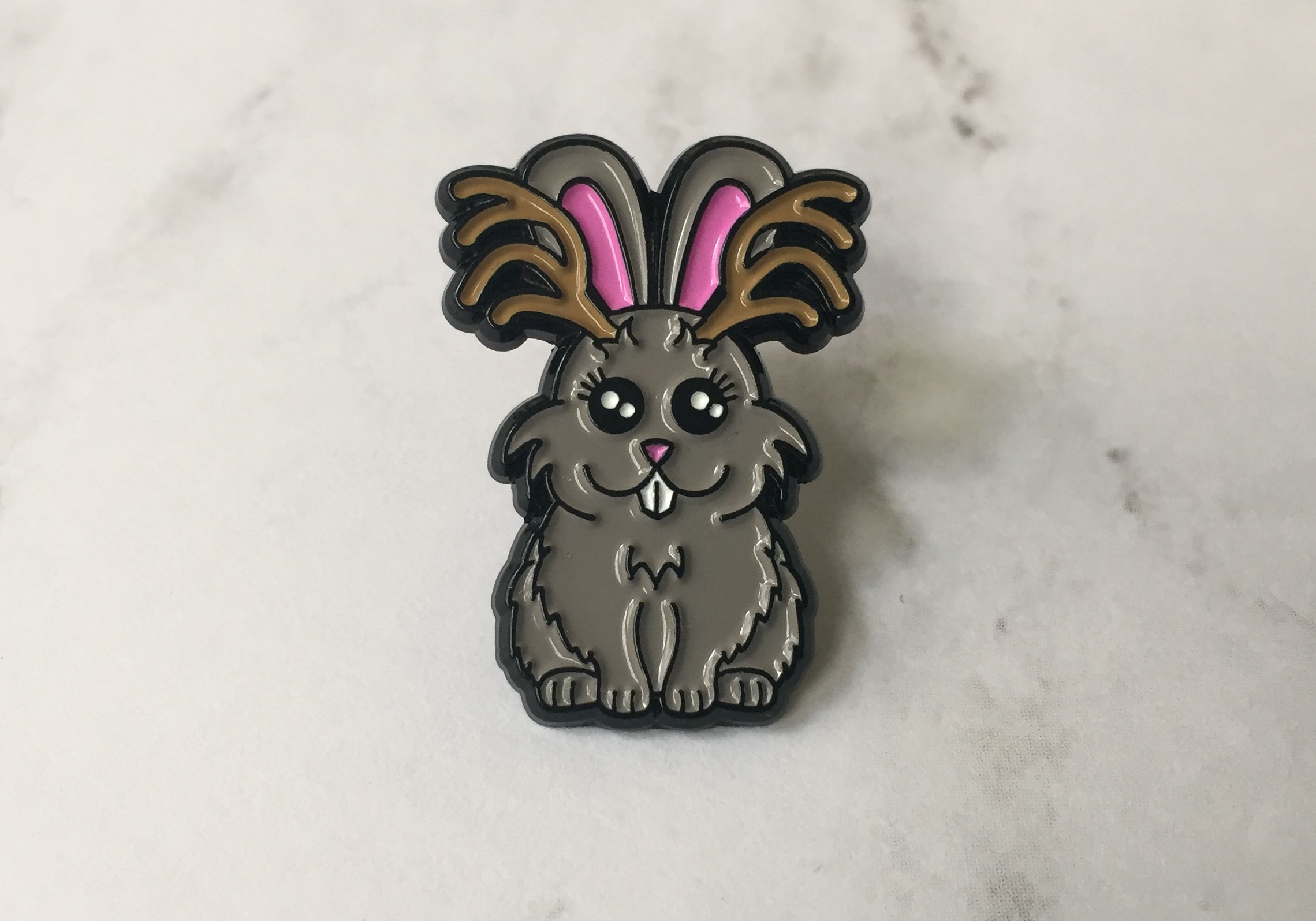 A colorful 1-inch soft enamel pin featuring a whimsical Jackalope design from the Cryptid Collection, showcasing intricate details and vibrant colors.