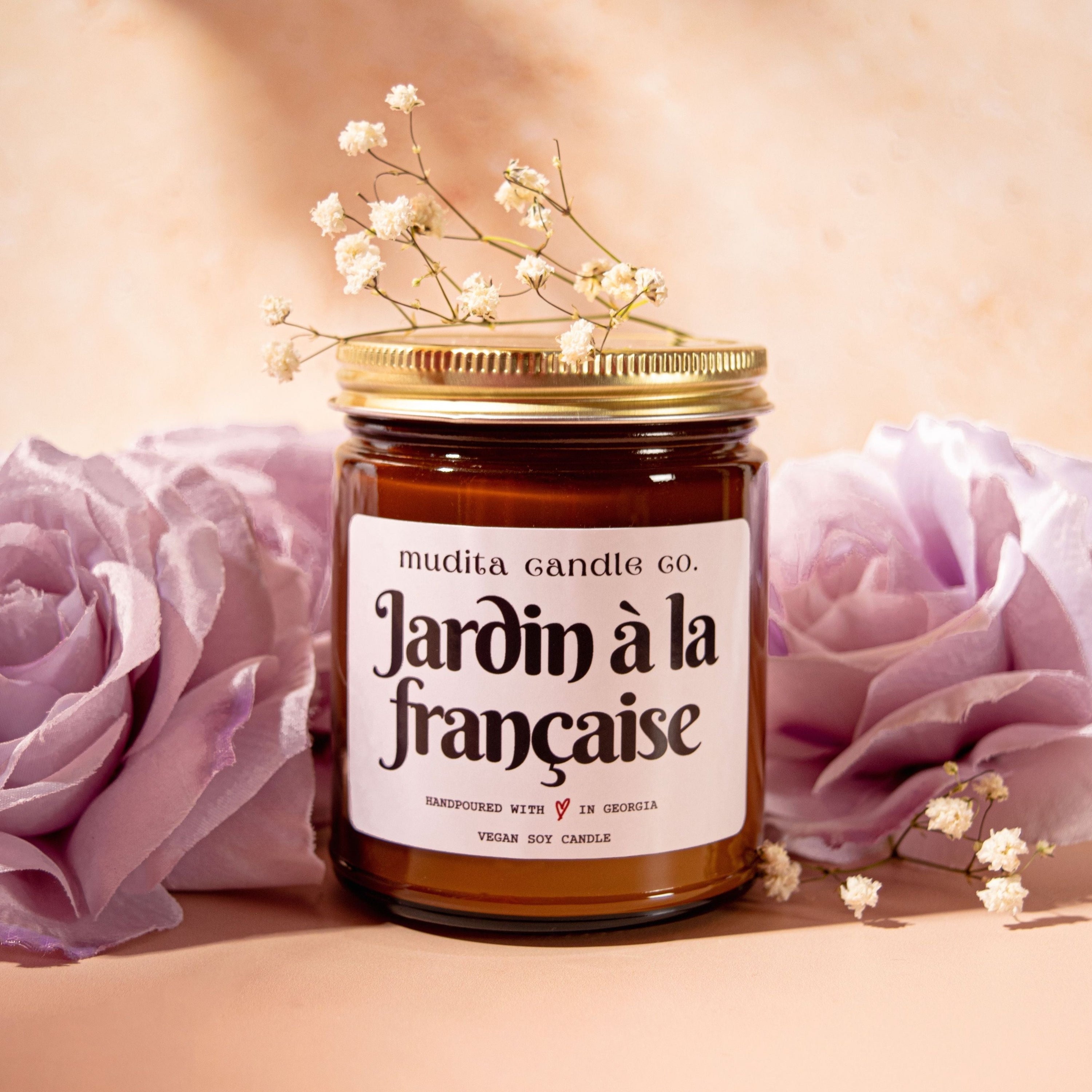 Jardin à la Française candle in a reusable amber glass jar with a gold lid, showcasing a blend of floral fragrances.