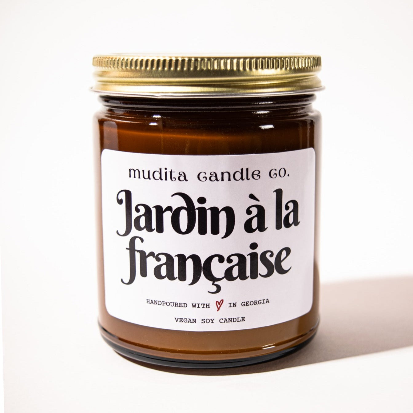 Jardin à la Française candle in a reusable amber glass jar with a gold lid, showcasing a blend of floral fragrances.