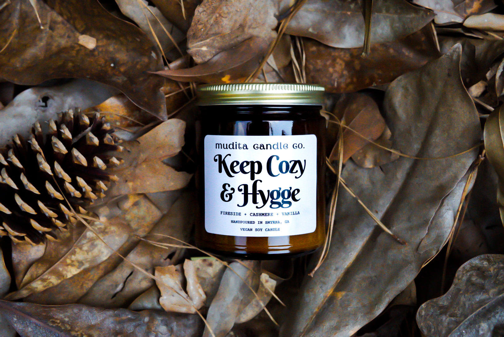 Keep Cozy & Hygge candle in amber glass jar with gold lid, featuring warm scents of fireside, cashmere, and vanilla.