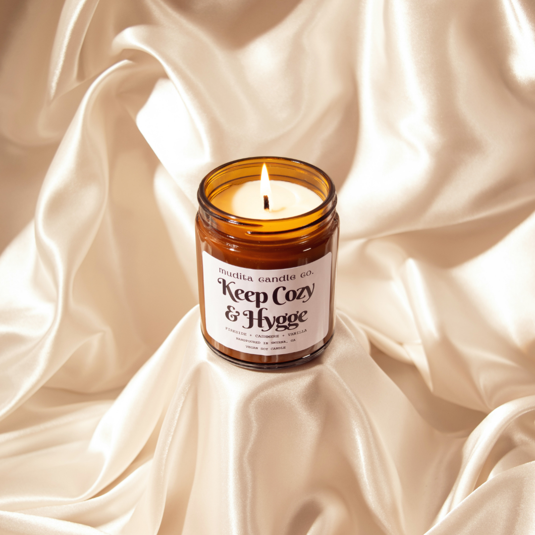 Keep Cozy & Hygge candle in amber glass jar with gold lid, featuring warm scents of fireside, cashmere, and vanilla.