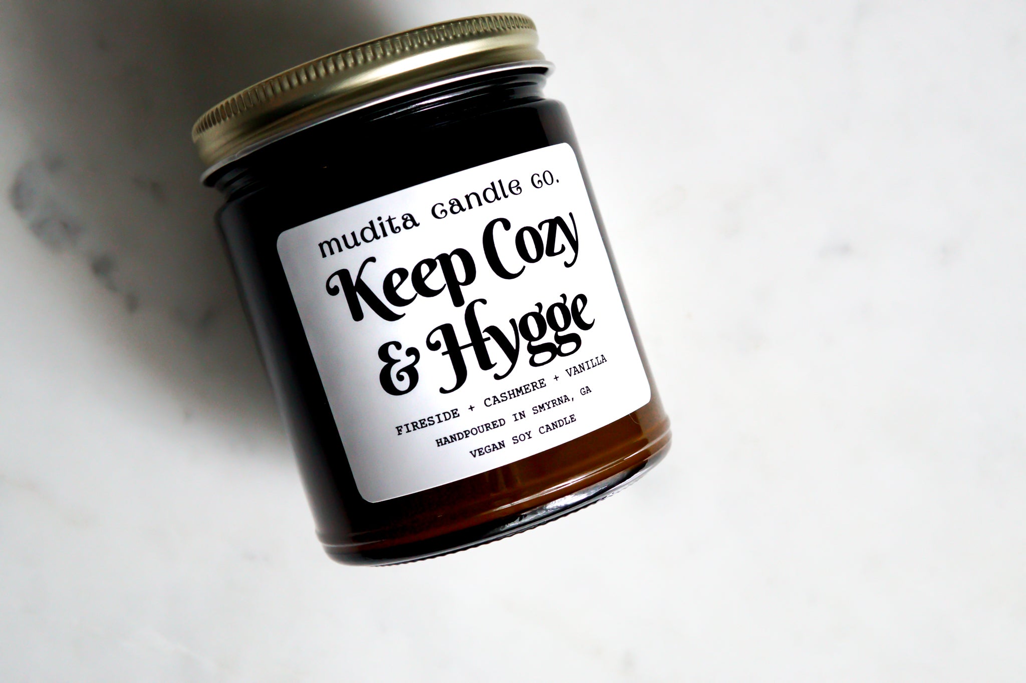 Keep Cozy & Hygge candle in amber glass jar with gold lid, featuring warm scents of fireside, cashmere, and vanilla.