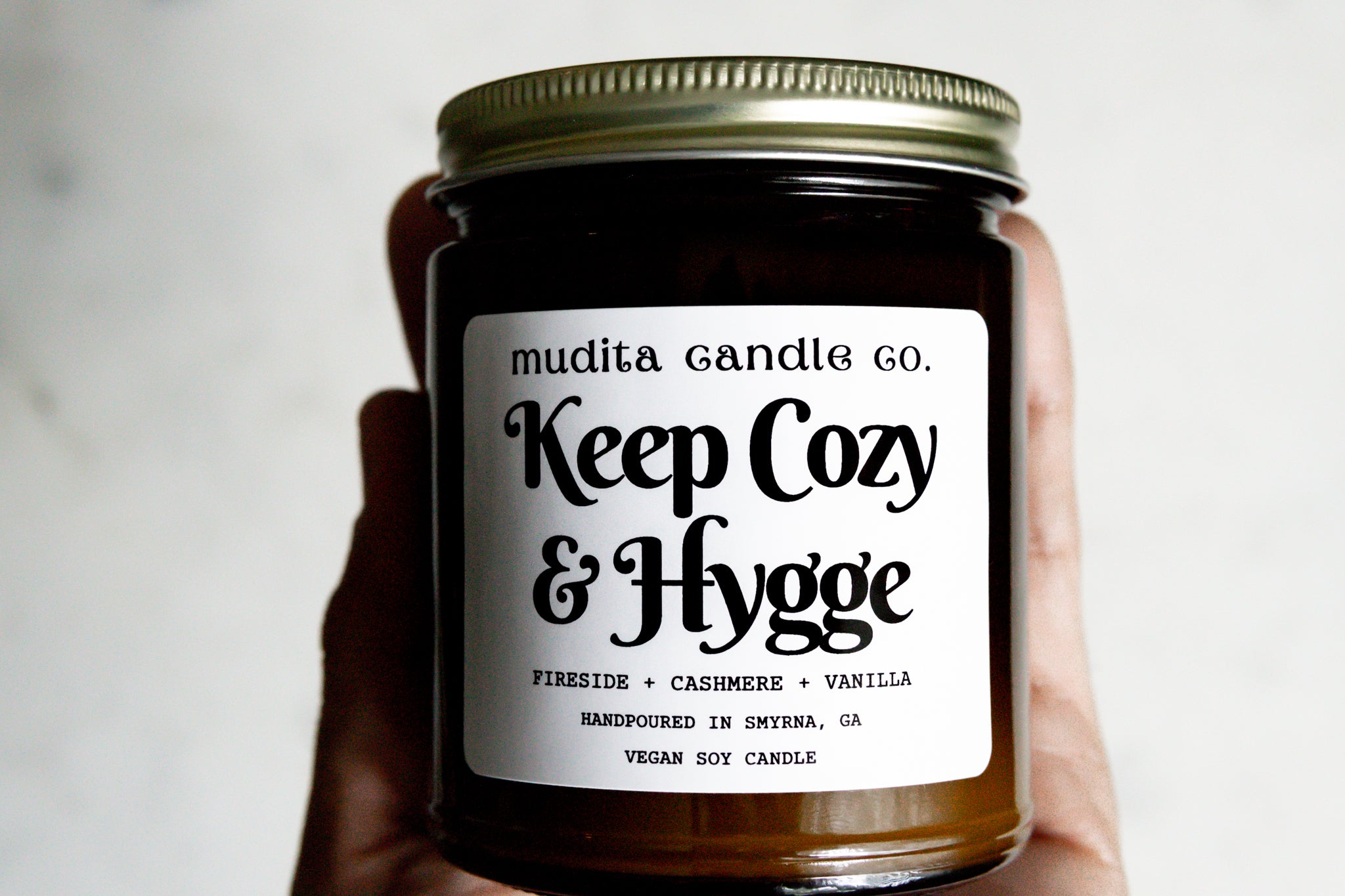 Keep Cozy & Hygge candle in amber glass jar with gold lid, featuring warm scents of fireside, cashmere, and vanilla.