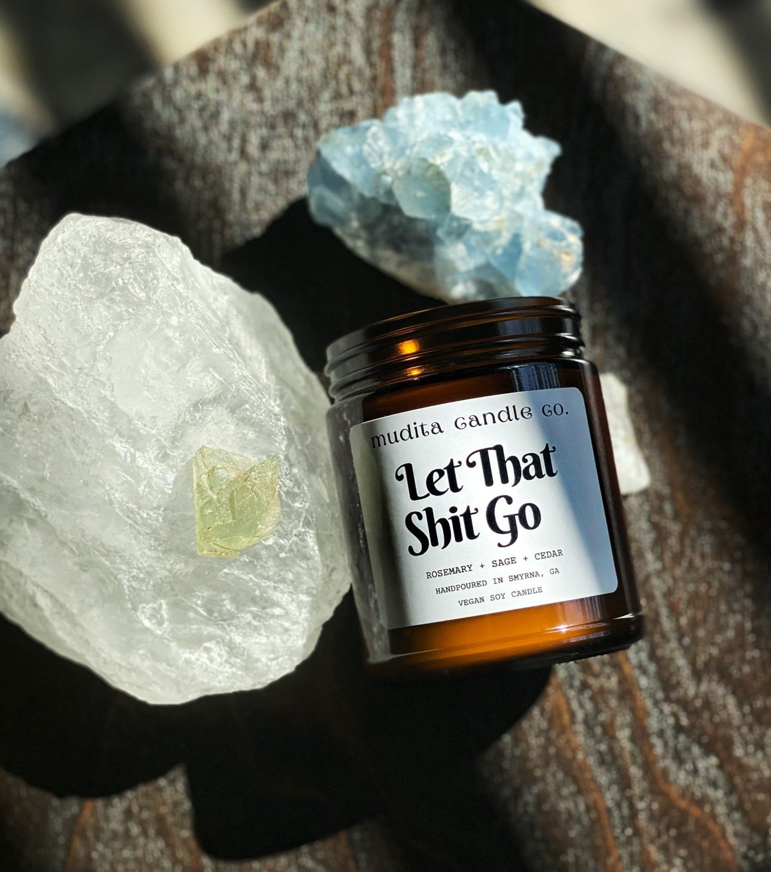 Let That Shit Go candle in amber glass jar with gold lid, featuring rosemary and sage scent.