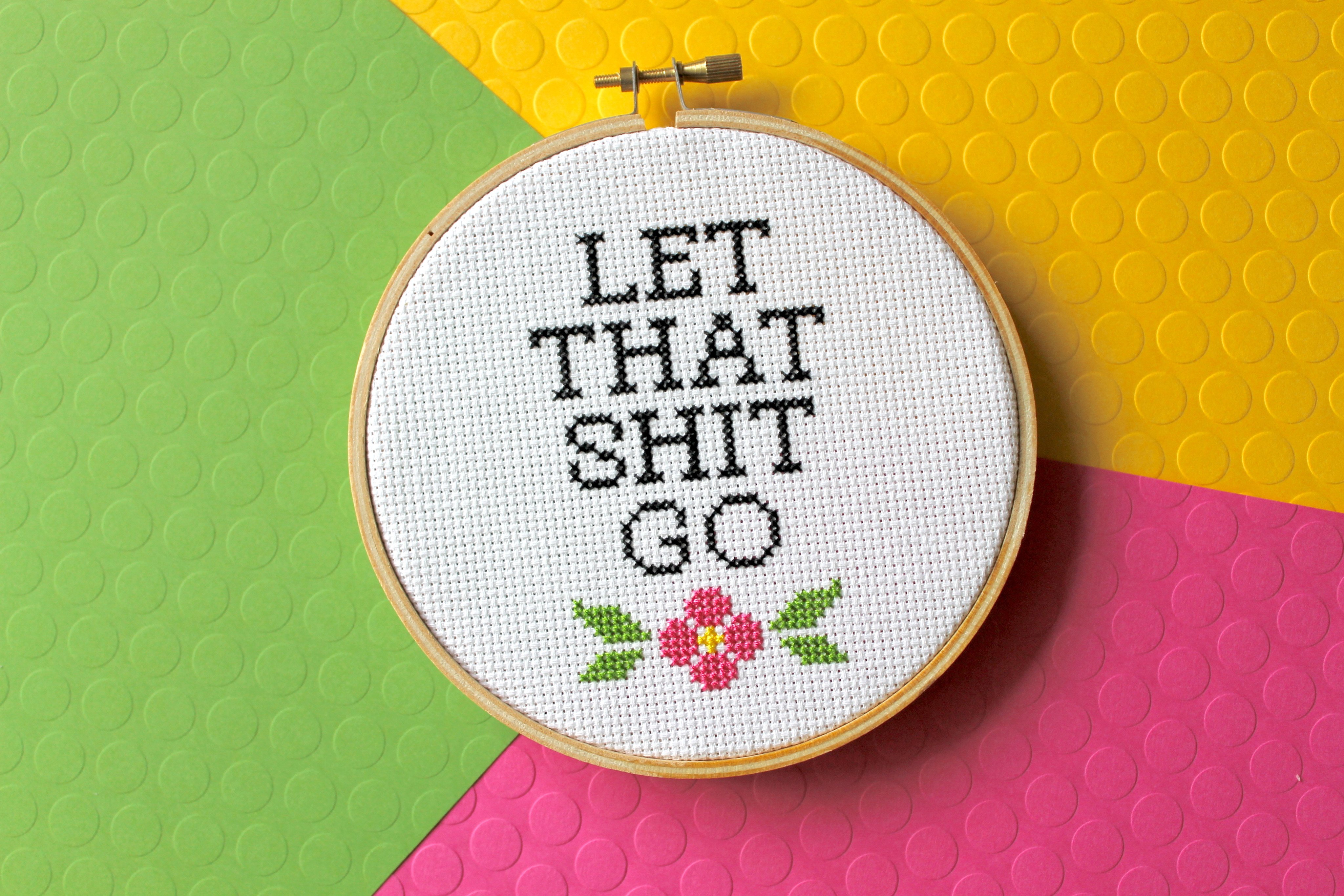 Let That Sh*t Go Counted Cross Stitch DIY Kit featuring floral elements and text, complete with all necessary supplies.