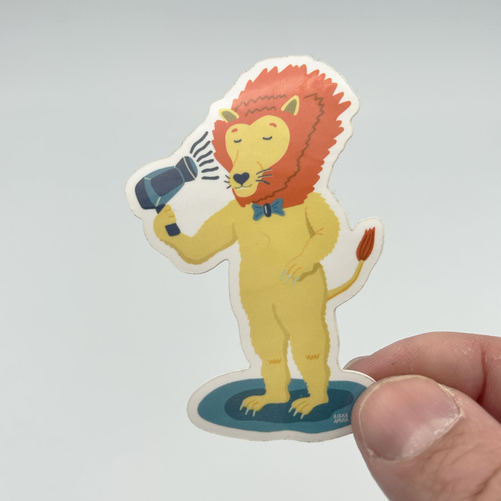 A colorful vinyl sticker featuring a lion blow-drying its mane, showcasing vibrant colors and a glossy finish.