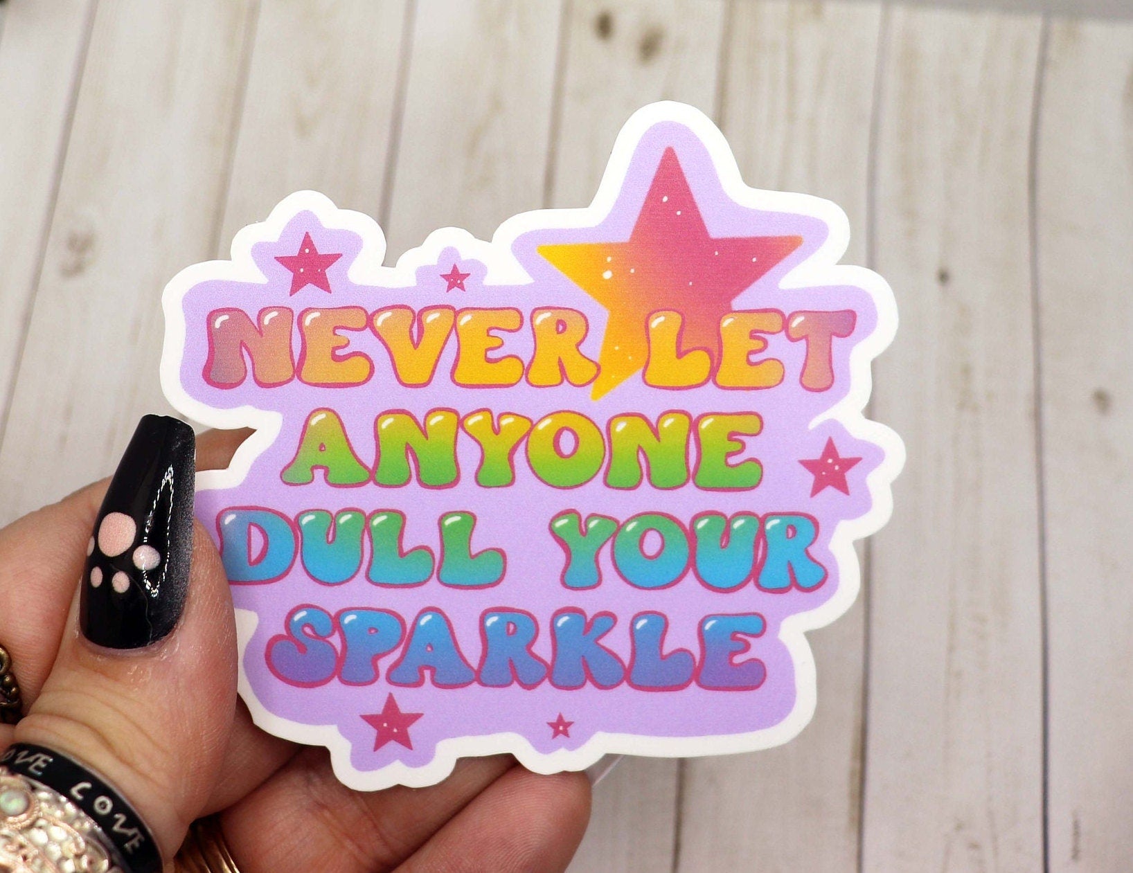 A vibrant vinyl sticker featuring the phrase 'Never Let Anyone Dull Your Sparkle' on a matte background, perfect for personalizing items.