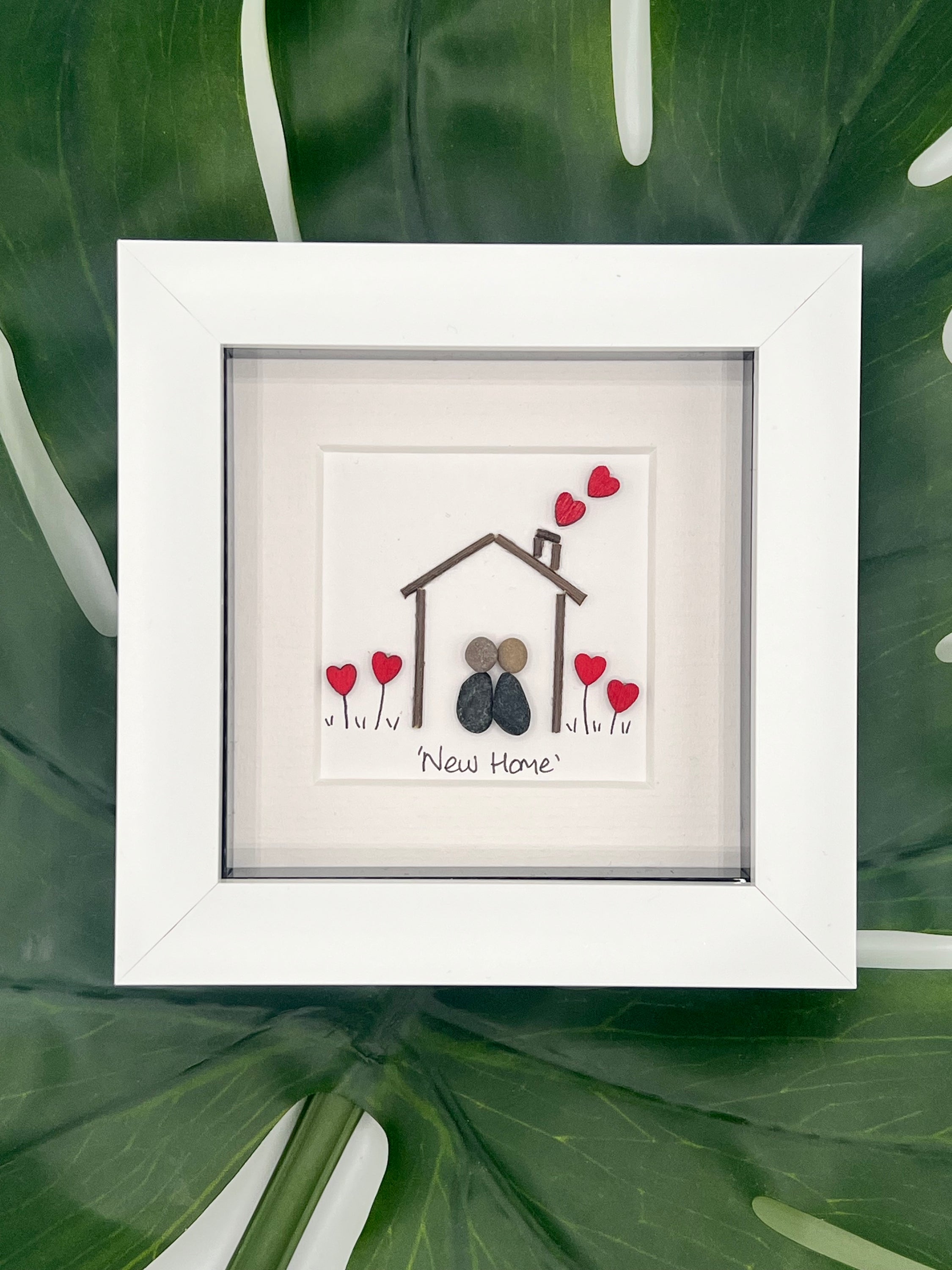 A beautifully framed pebble art picture symbolizing a new home, featuring natural pebbles arranged artistically.