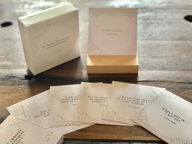 A beautifully designed set of Oh Happy Life affirmation cards displayed with a stylish card stand, featuring positive messages for daily inspiration.