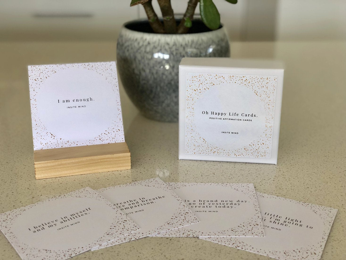 A beautifully designed set of Oh Happy Life affirmation cards displayed with a stylish card stand, featuring positive messages for daily inspiration.