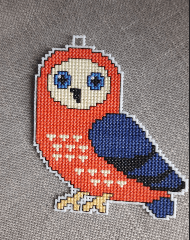 A counted cross-stitch kit featuring owls, including plastic canvas, colorful threads, and instructions.