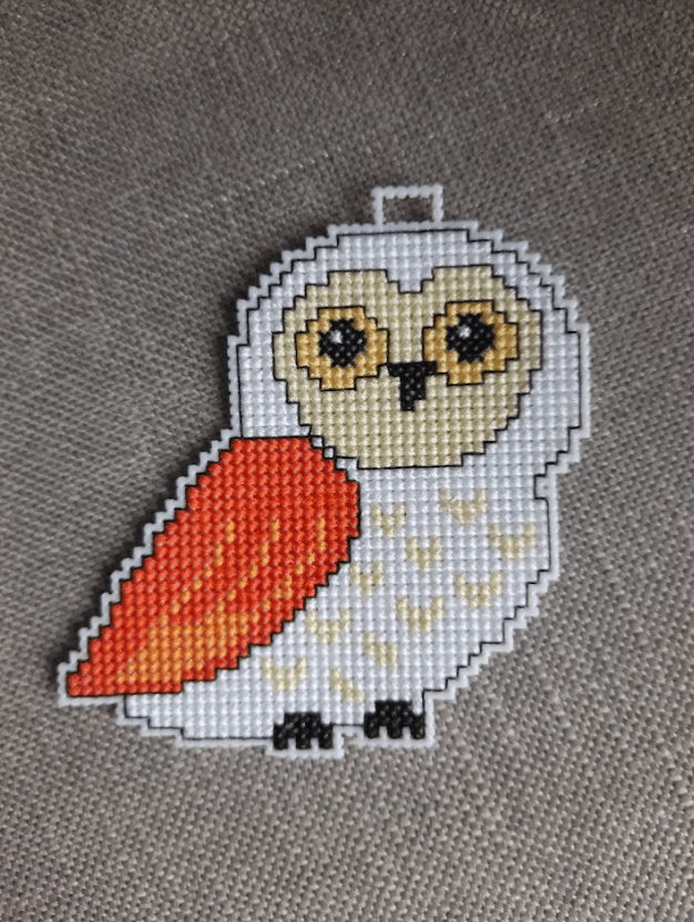 A counted cross-stitch kit featuring owls, including plastic canvas, colorful threads, and instructions.