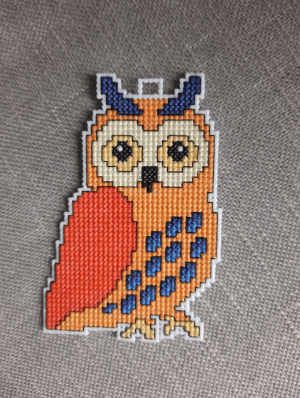 A counted cross-stitch kit featuring owls, including plastic canvas, colorful threads, and instructions.