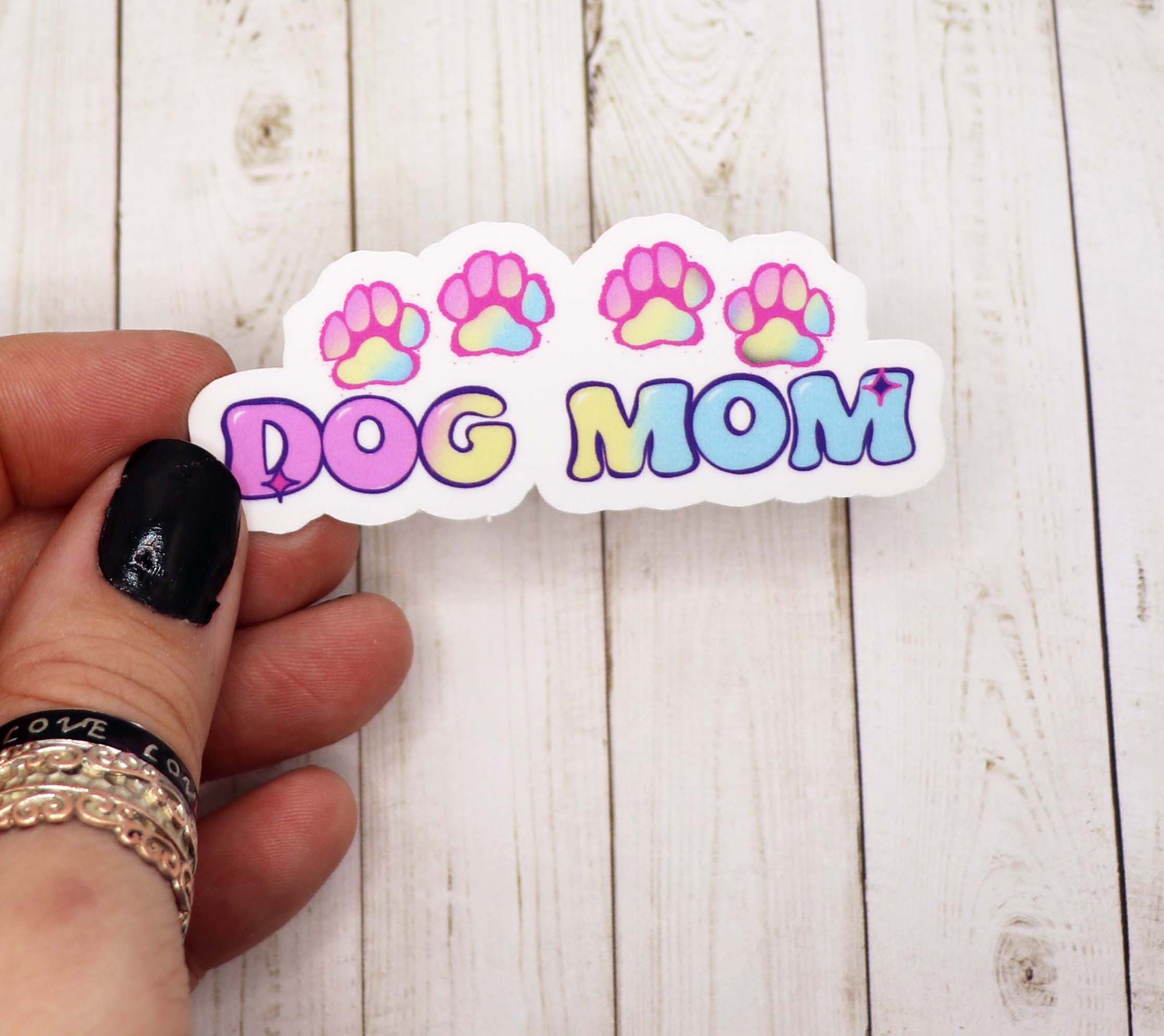 A pastel-colored sticker that reads 'Dog Mom', featuring playful dog-themed graphics, perfect for personalizing items.