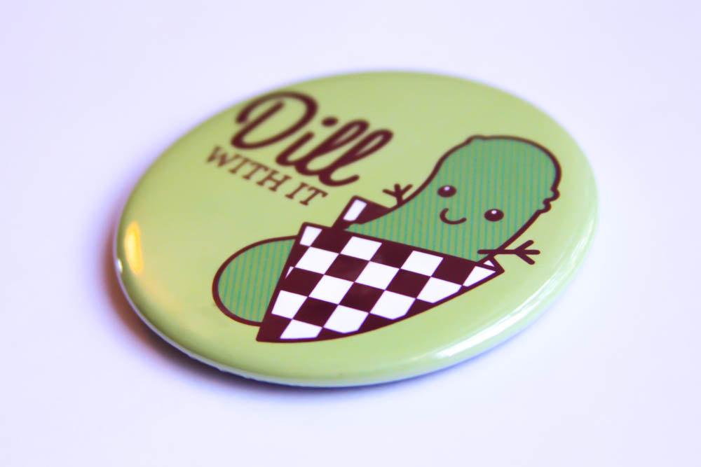 A cheerful 'Dill With It!' pickle magnet and pin featuring a happy pickle character and vibrant colors.