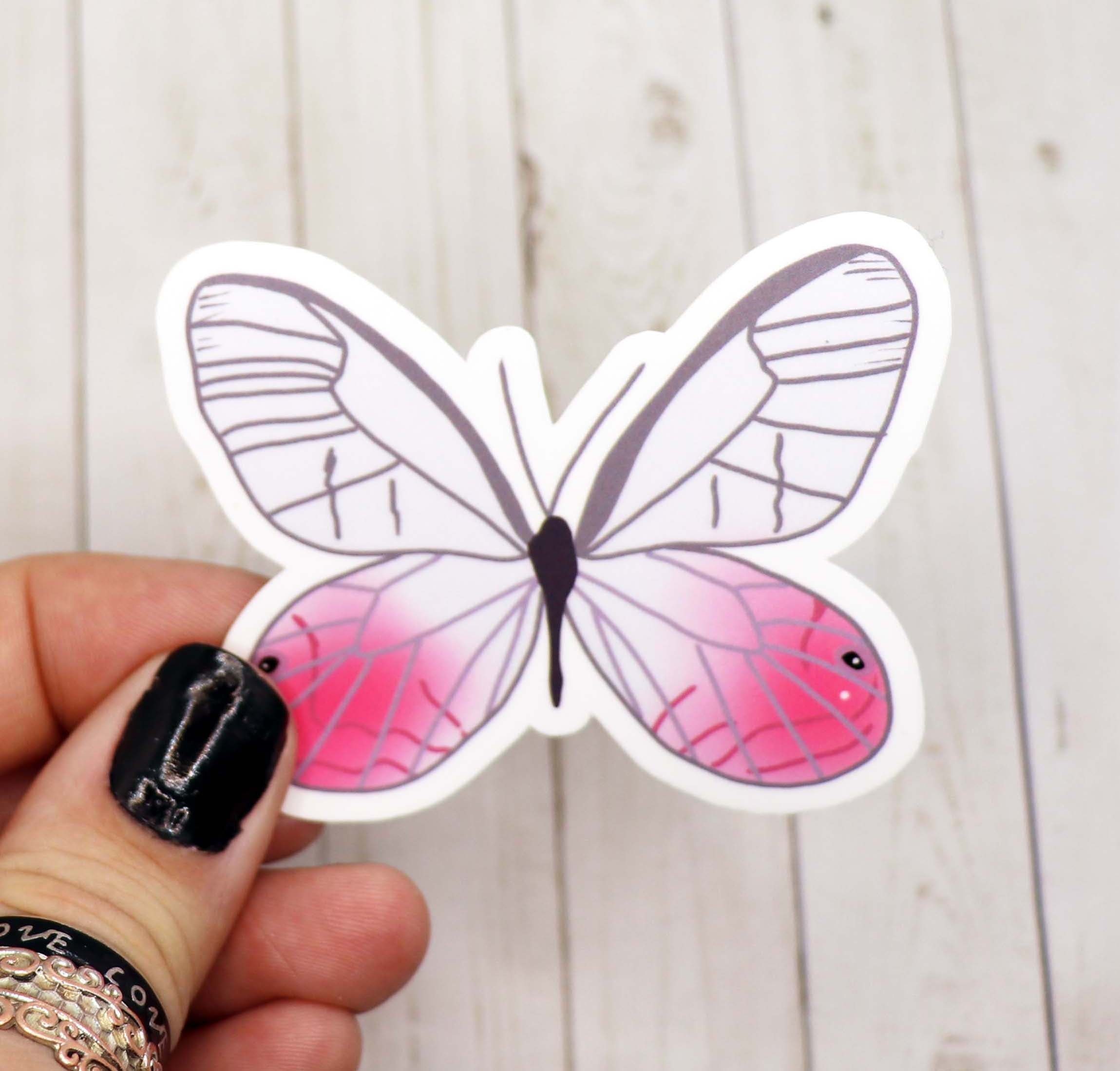 A vibrant pink and white butterfly sticker on a matte vinyl surface, showcasing intricate details and a whimsical design.